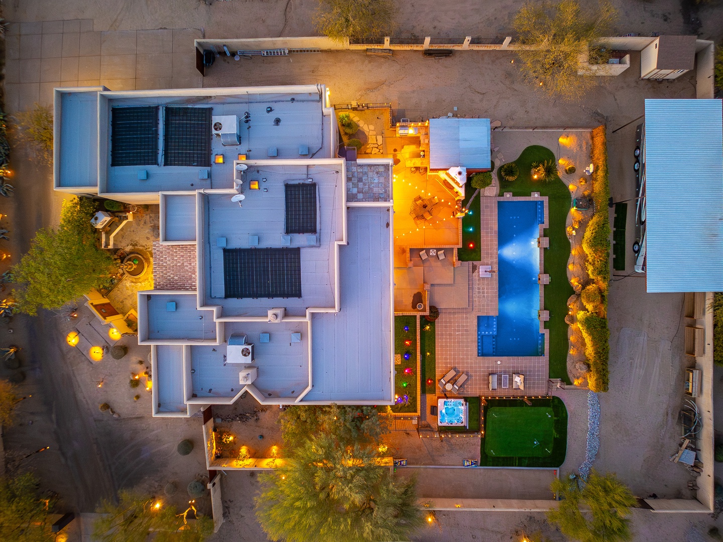 An aerial view reveals the property's elegant layout, featuring a sparkling swimming pool, sun-drenched terraces, lush garden areas, and ambient outdoor lighting creating an inviting atmosphere at dusk.
