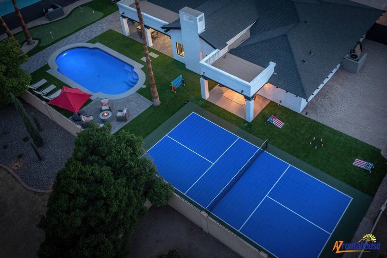 Aerial view of modern vacation rental featuring private pool, tennis court, and contemporary architecture with landscaped grounds.