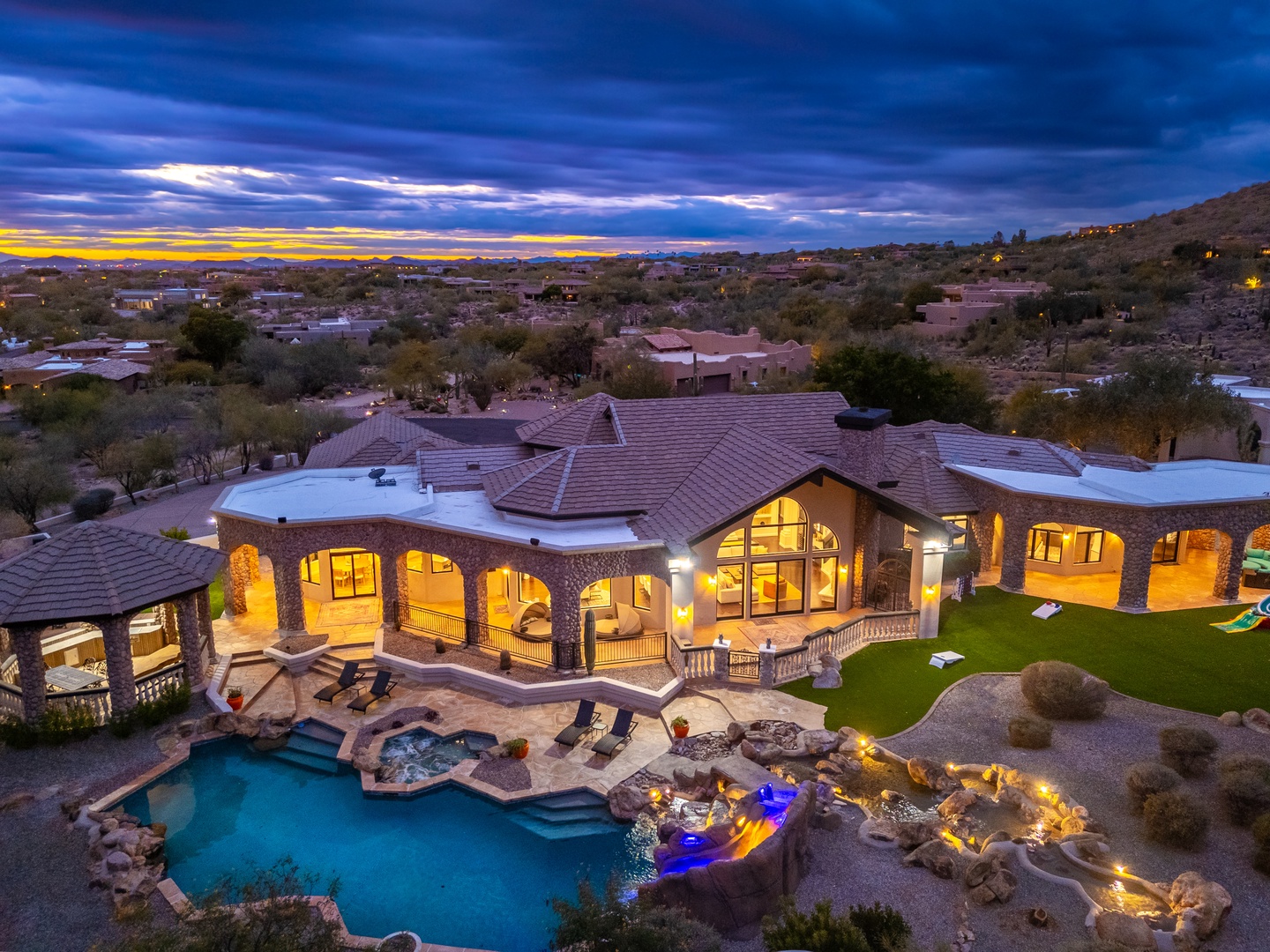 Stunning desert estate nestled in the hills, featuring resort-style pool, spa, and expansive outdoor entertaining areas beneath dramatic Arizona skies at twilight.