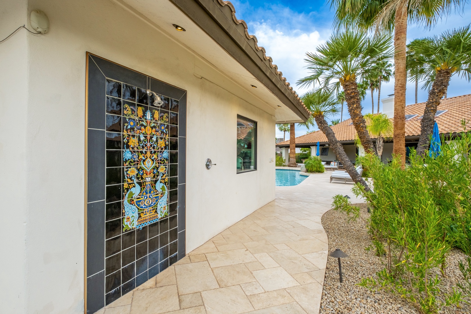 This property showcases a Mediterranean-style exterior with decorative tile artwork, lush palm trees, and a sparkling pool area perfect for desert retreat relaxation.
