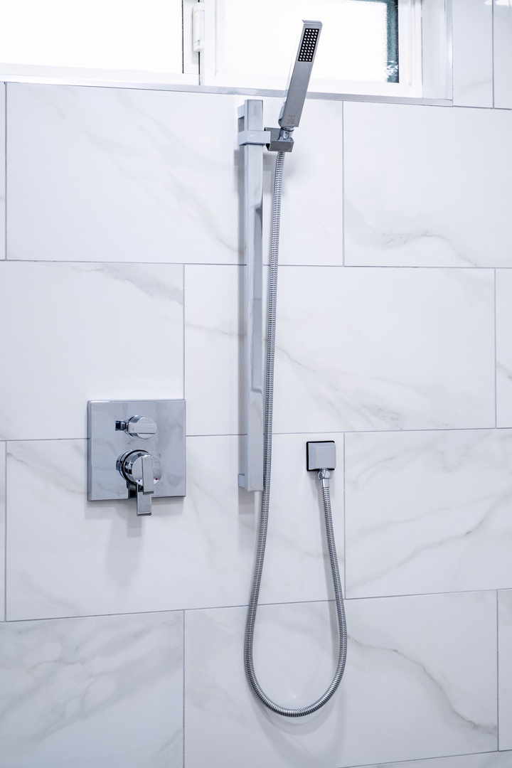 Step into your private spa-like retreat with a sleek rainfall showerhead and modern fixtures set against elegant marble-inspired tile.