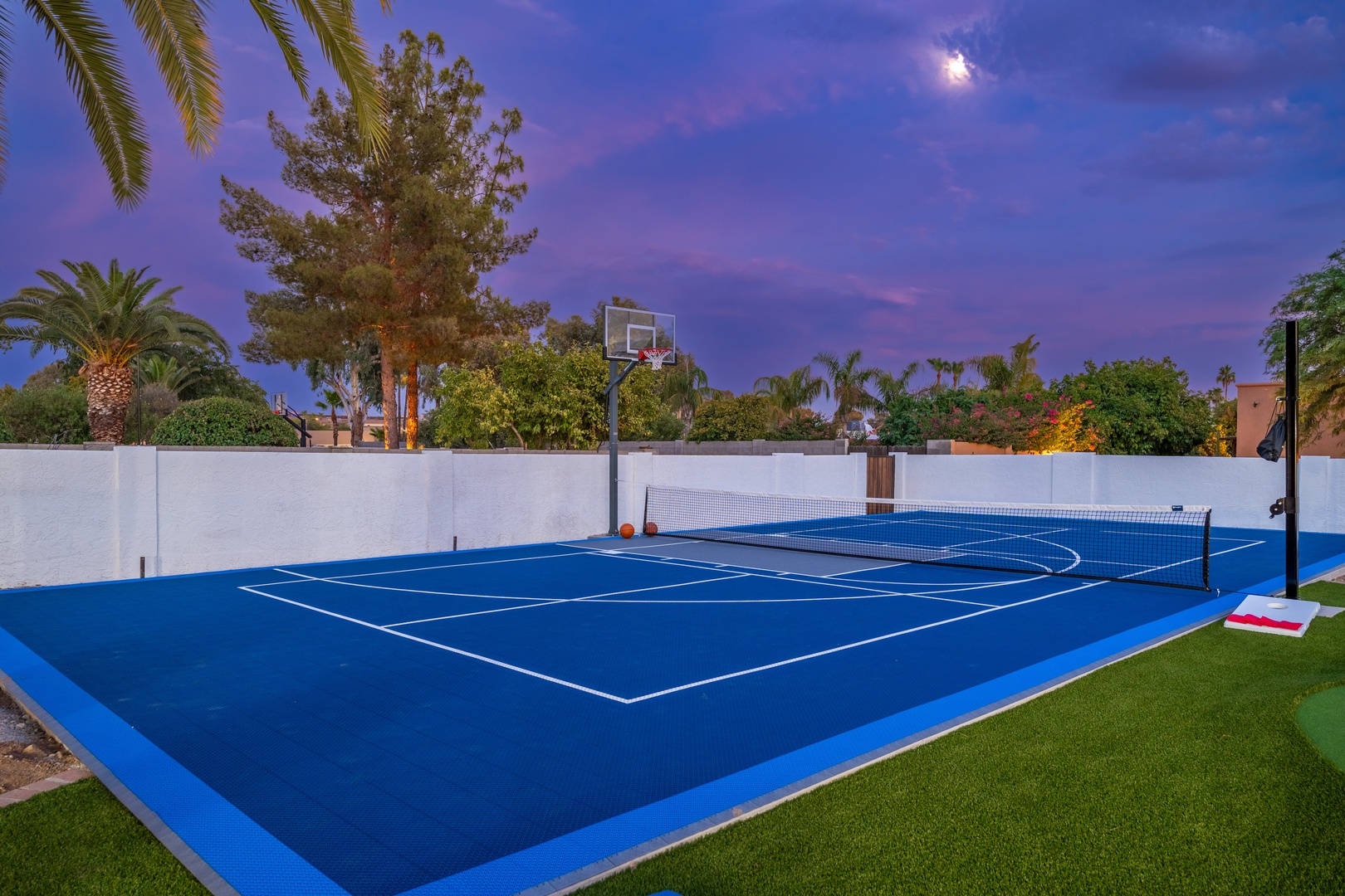 A versatile sport court surrounded by palm trees and lush landscaping, offering tennis, basketball, and pickleball beneath stunning twilight skies.