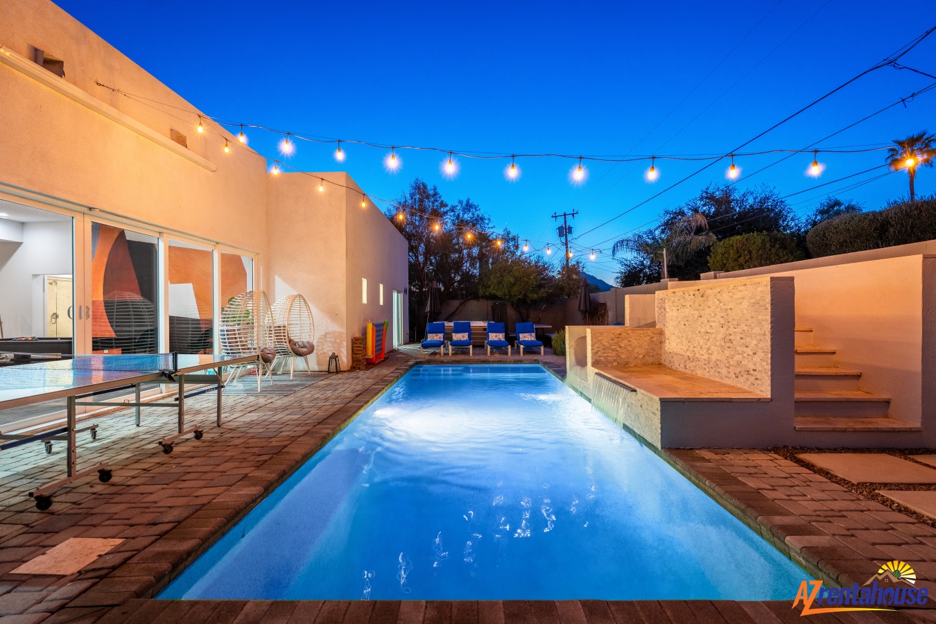 Elegant outdoor pool area features sparkling blue water, comfortable seating, and charming string lights overhead creating magical evening ambiance.