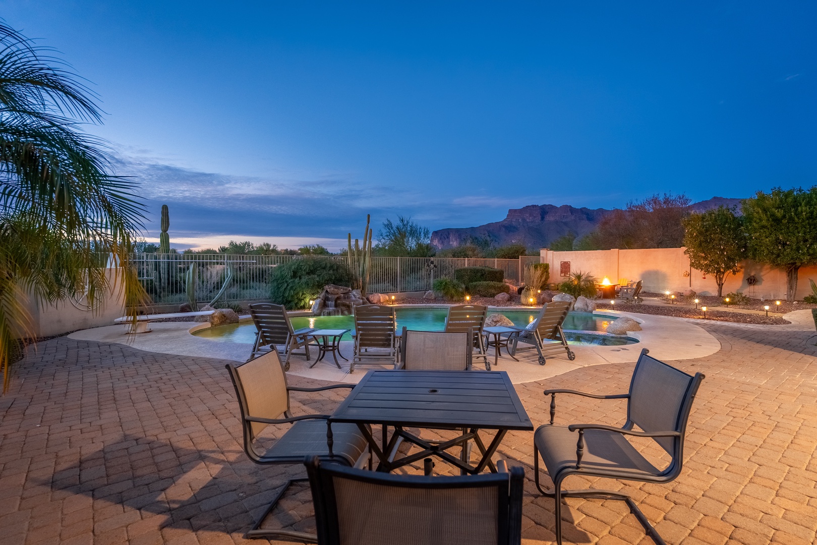 Stunning desert resort patio with pool, mountain backdrop, and illuminated evening ambiance perfect for outdoor relaxation and gatherings.