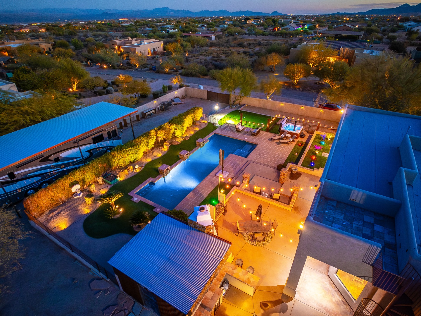 Aerial view of a stunning desert property at twilight, showcasing dual pools, outdoor entertaining spaces, and mountain backdrops. The resort-style layout sits amid the scenic Arizona landscape, illuminated by ambient evening lighting and surrounded by na