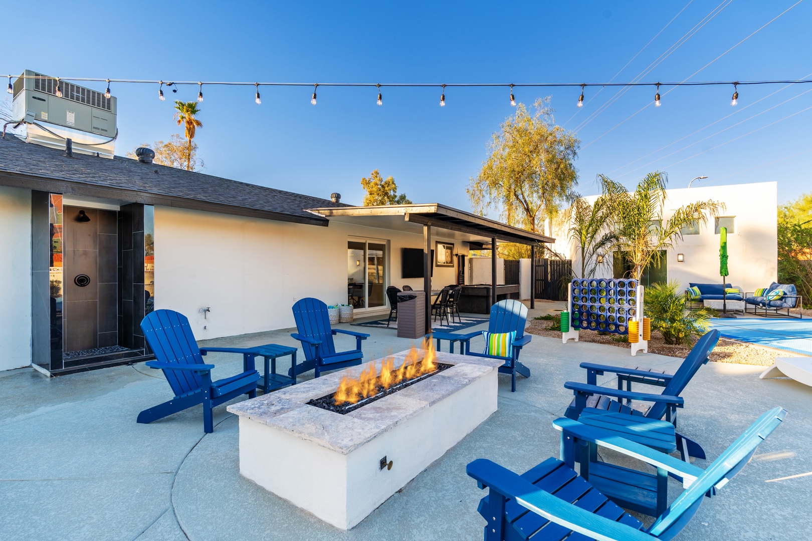 Picture yourself relaxing in these comfortable blue Adirondack chairs around the modern fire pit, with string lights twinkling overhead as the sun sets. This inviting outdoor space is perfect for gathering and unwinding.