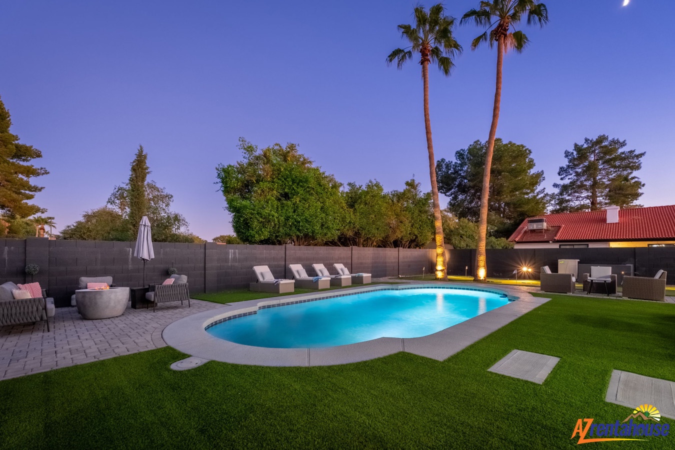 Stunning backyard oasis with sparkling pool surrounded by manicured lawn and towering palms, lit beautifully for magical twilight evenings.