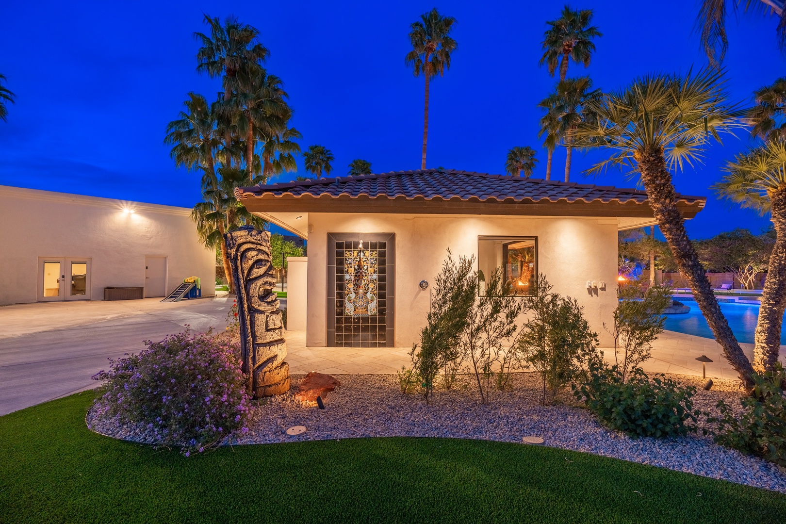 This elegant entrance welcomes guests with resort-style landscaping, illuminated palm trees, and a charming courtyard that sets the tone for a memorable desert retreat.