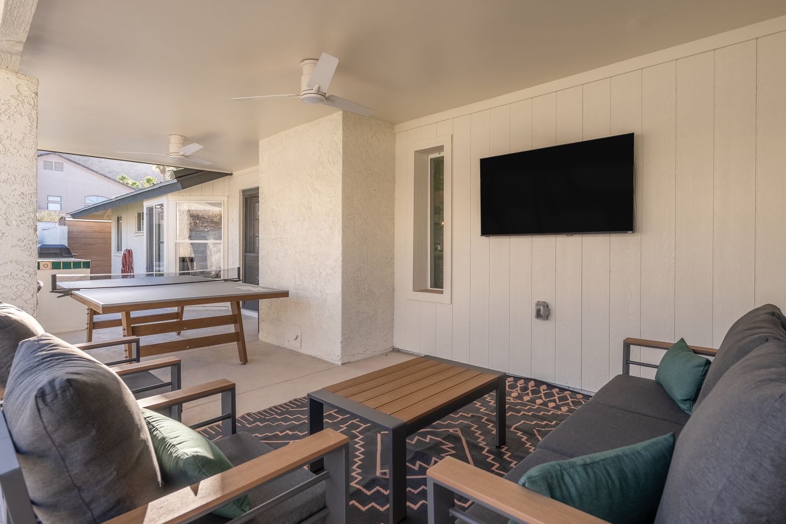 Relax in your covered patio with cozy seating, a wall-mounted TV, and a dining table—perfect for unwinding after exploring or enjoying meals outdoors.