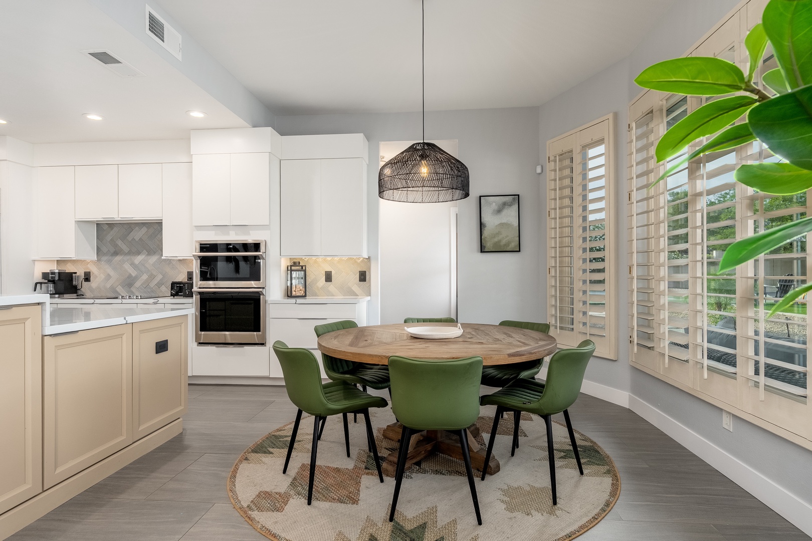 Gather around your dining table in this bright, open space where the modern kitchen meets warm wood tones and pops of green, perfect for morning coffee or evening meals together.