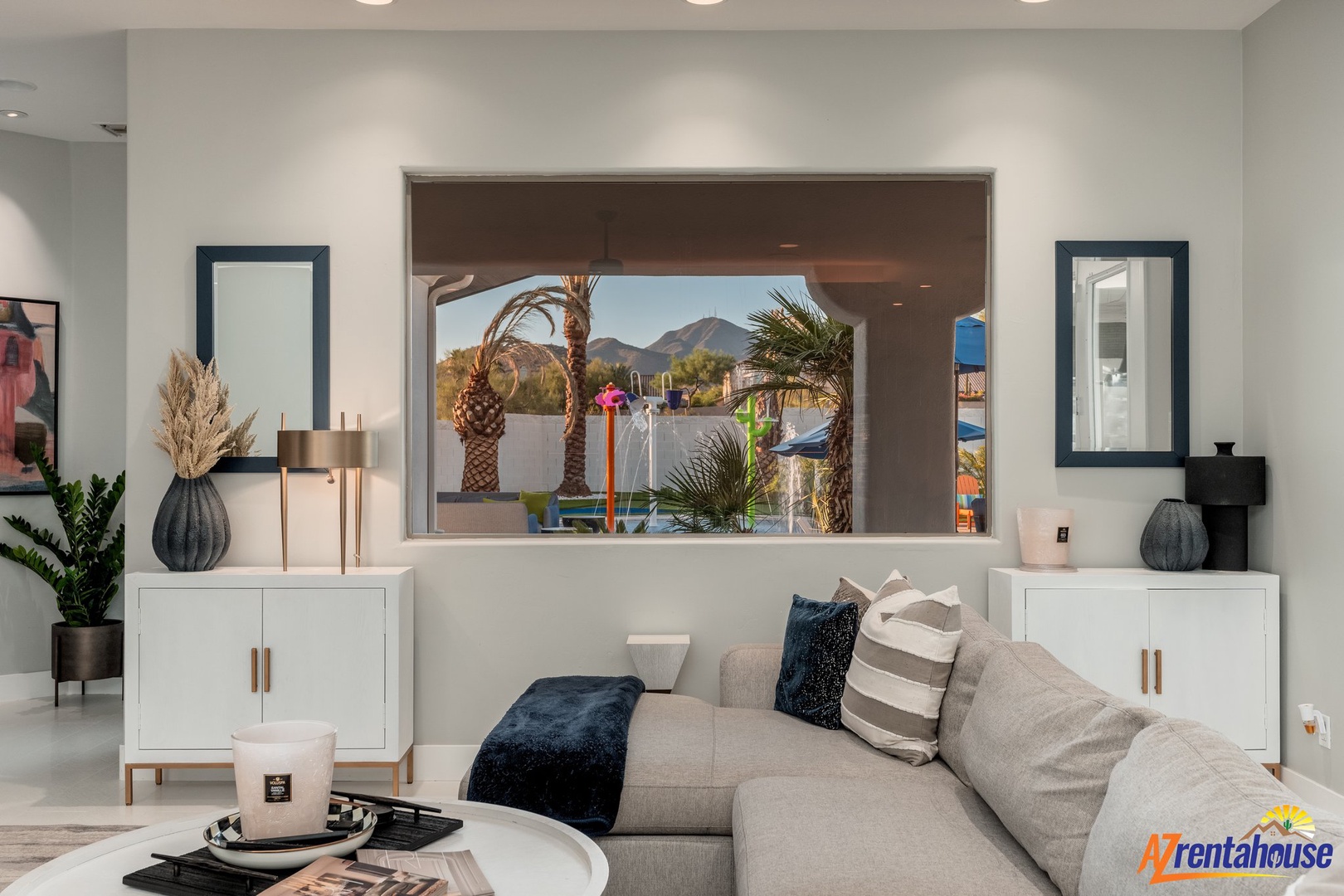 Relax in your stylish living room where a picture window frames tropical palm trees and mountains beyond.
