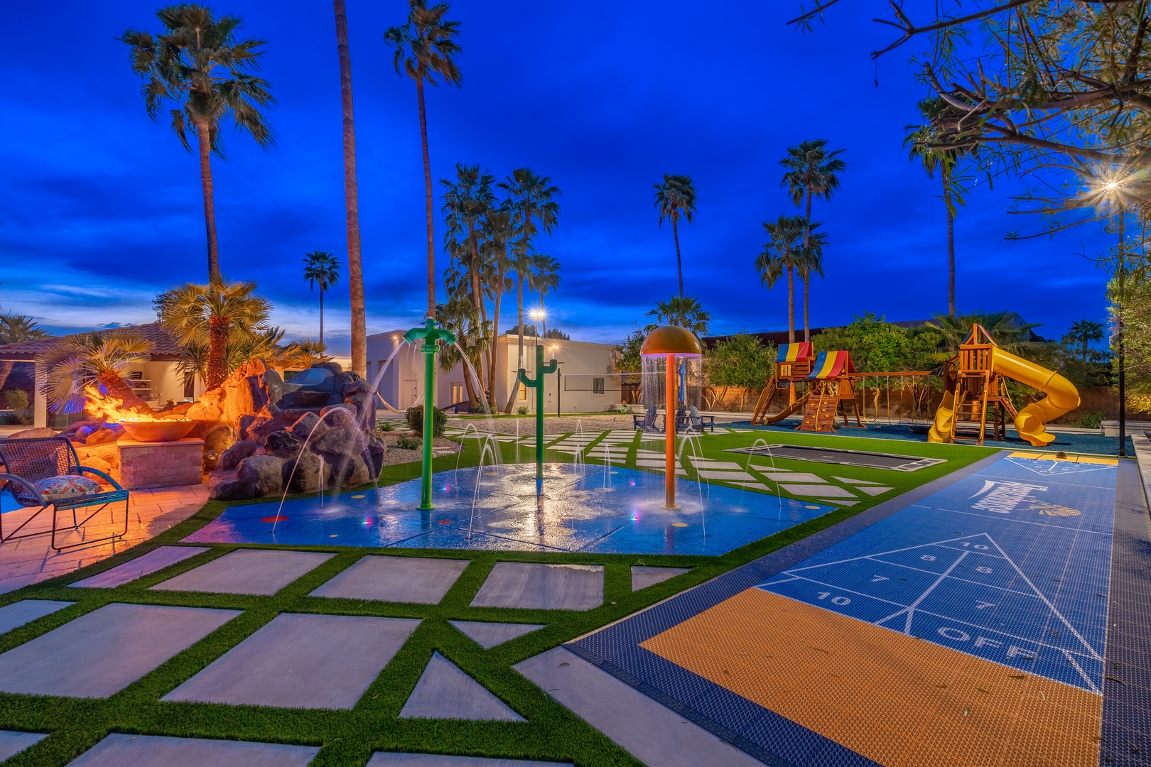 A resort-style backyard features splash pads, colorful play structures, and towering palms under a stunning twilight sky—an entertainer's dream designed for family fun.