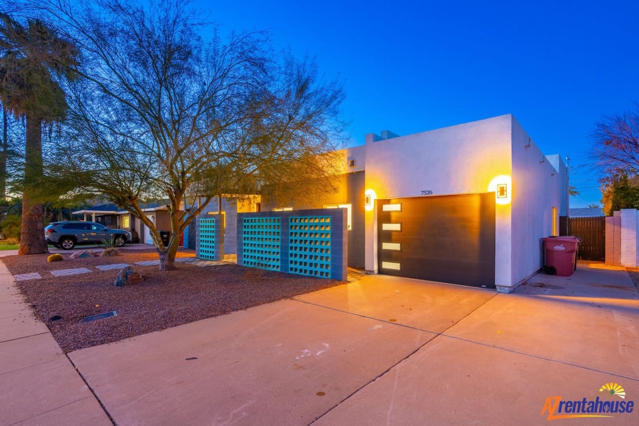 Modern desert home with striking turquoise accents and warm lighting creates a welcoming arrival experience in this peaceful neighborhood.