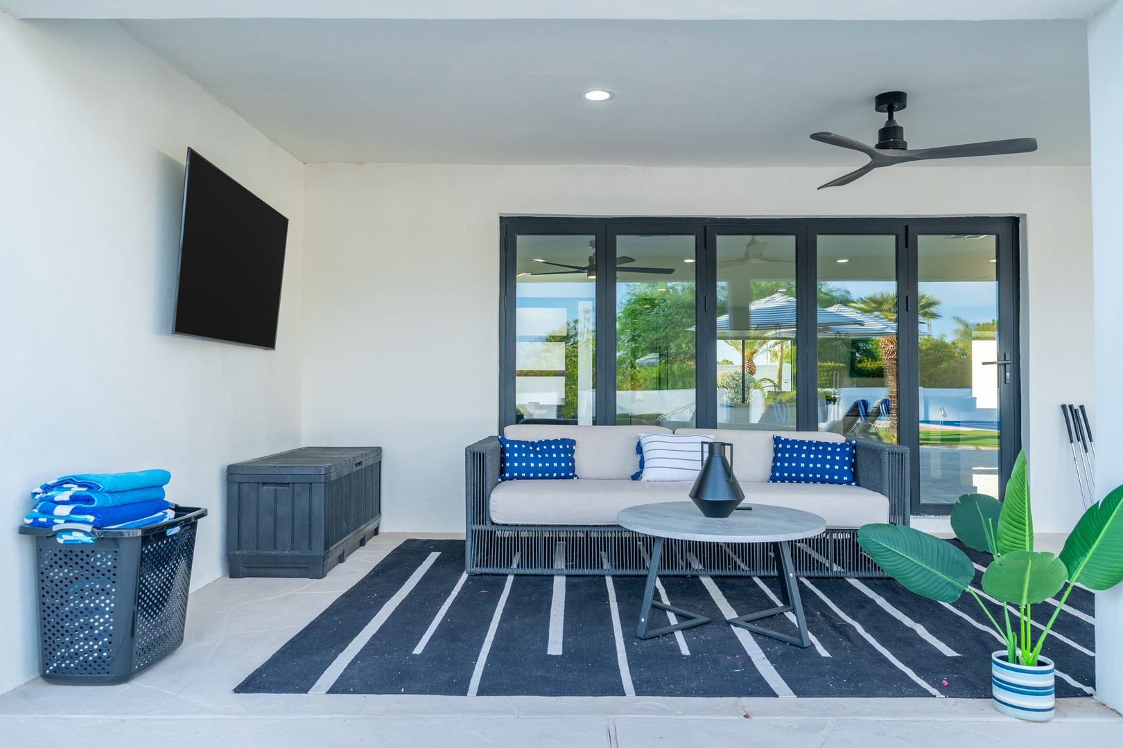 Unwind in your covered outdoor lounge, complete with plush seating, a ceiling fan to keep you cool, and a TV for entertainment. Just steps away, the sparkling pool awaits, framed by lush greenery and coastal palms.
