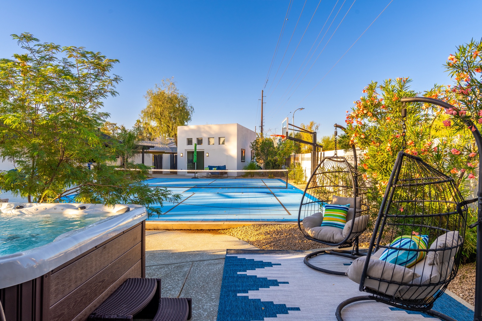 Picture yourself swaying gently in a cozy egg chair, sipping your favorite drink beside the sparkling hot tub and pool, surrounded by lush greenery and vibrant blooms under a brilliant blue sky.