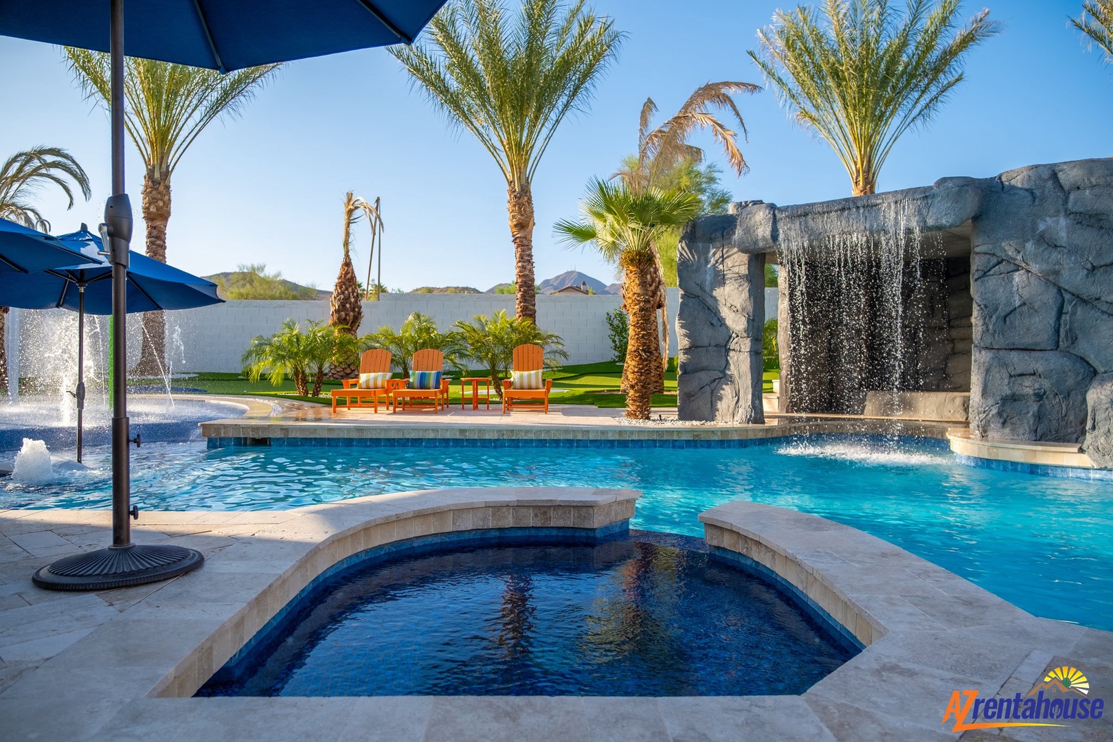 Tropical paradise with sparkling pool, stone waterfall, and orange loungers under swaying palms - your private desert retreat awaits.