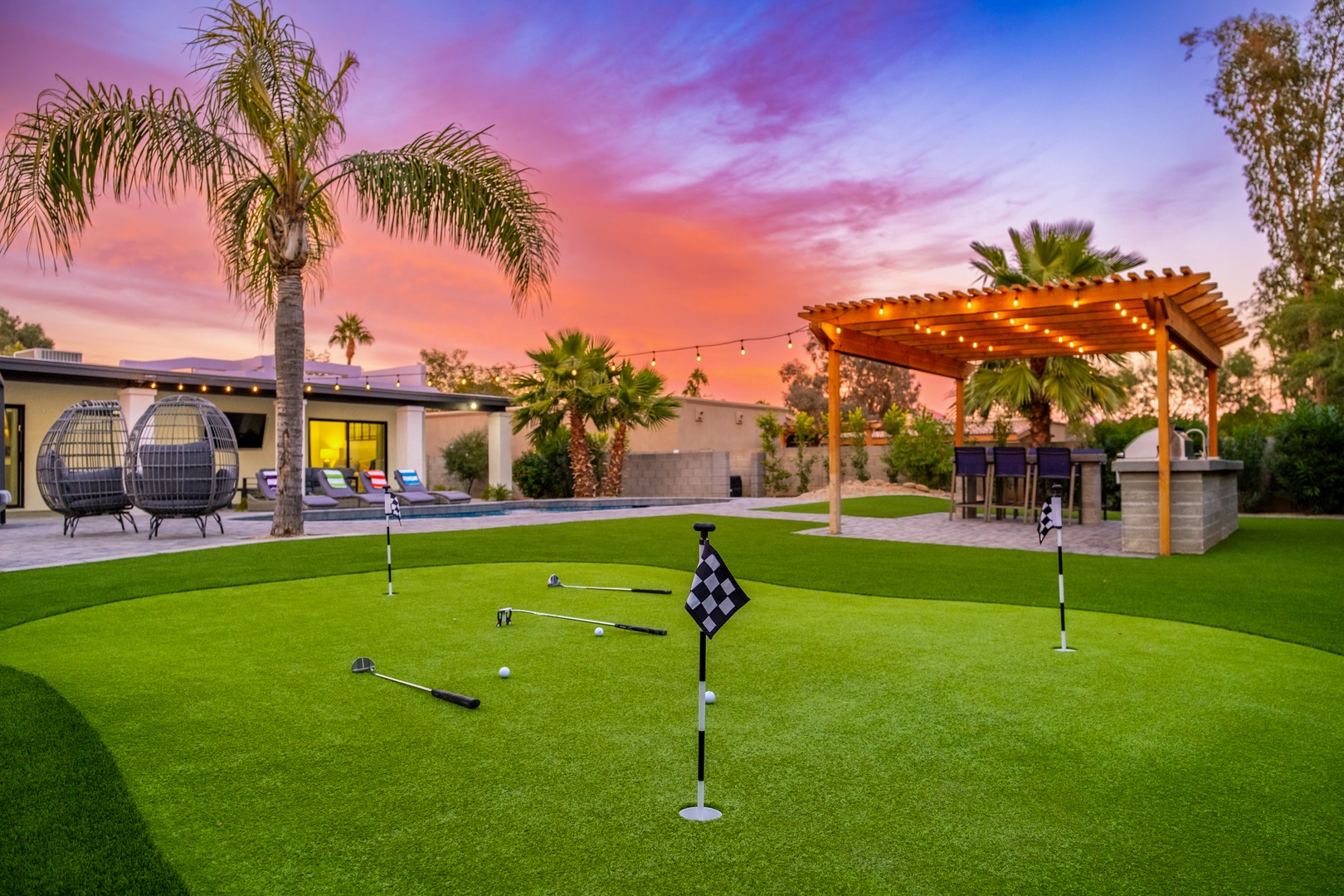 A stunning desert oasis captured at sunset, with a private putting green and outdoor entertaining areas surrounded by palms and dramatic sky.