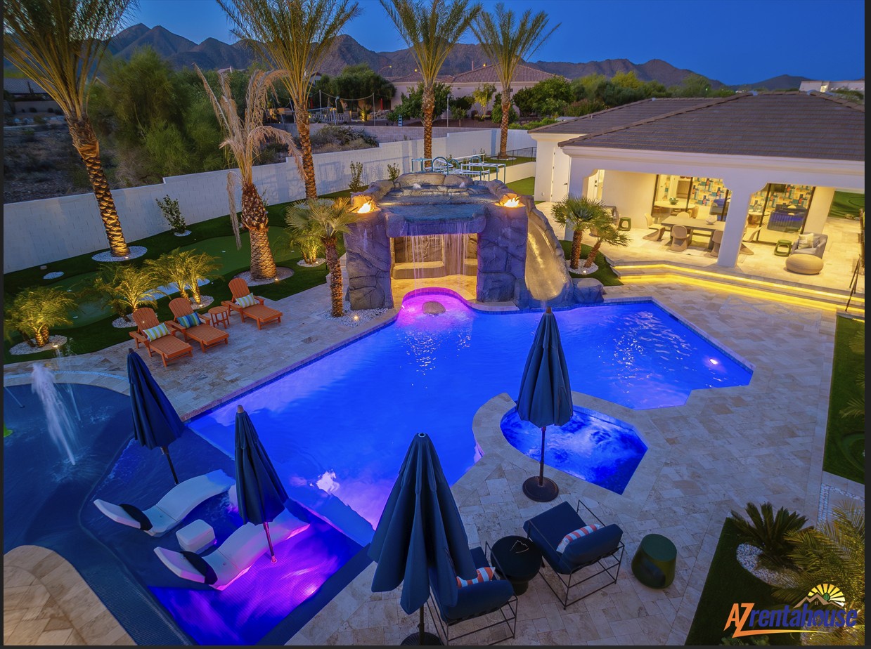 Desert luxury estate featuring illuminated resort-style pool with spa, waterfall, and mountain backdrop at twilight.