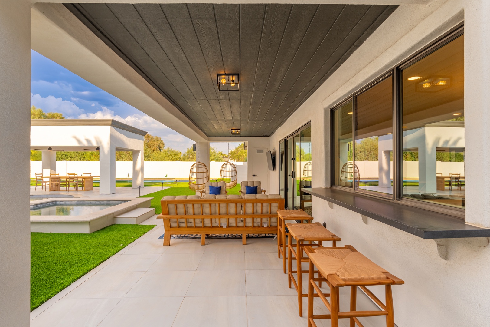Step into your covered outdoor oasis with stylish seating, where morning coffee or sunset cocktails become unforgettable moments. Beyond awaits lush lawn and a sparkling pool, perfect for your dream getaway.