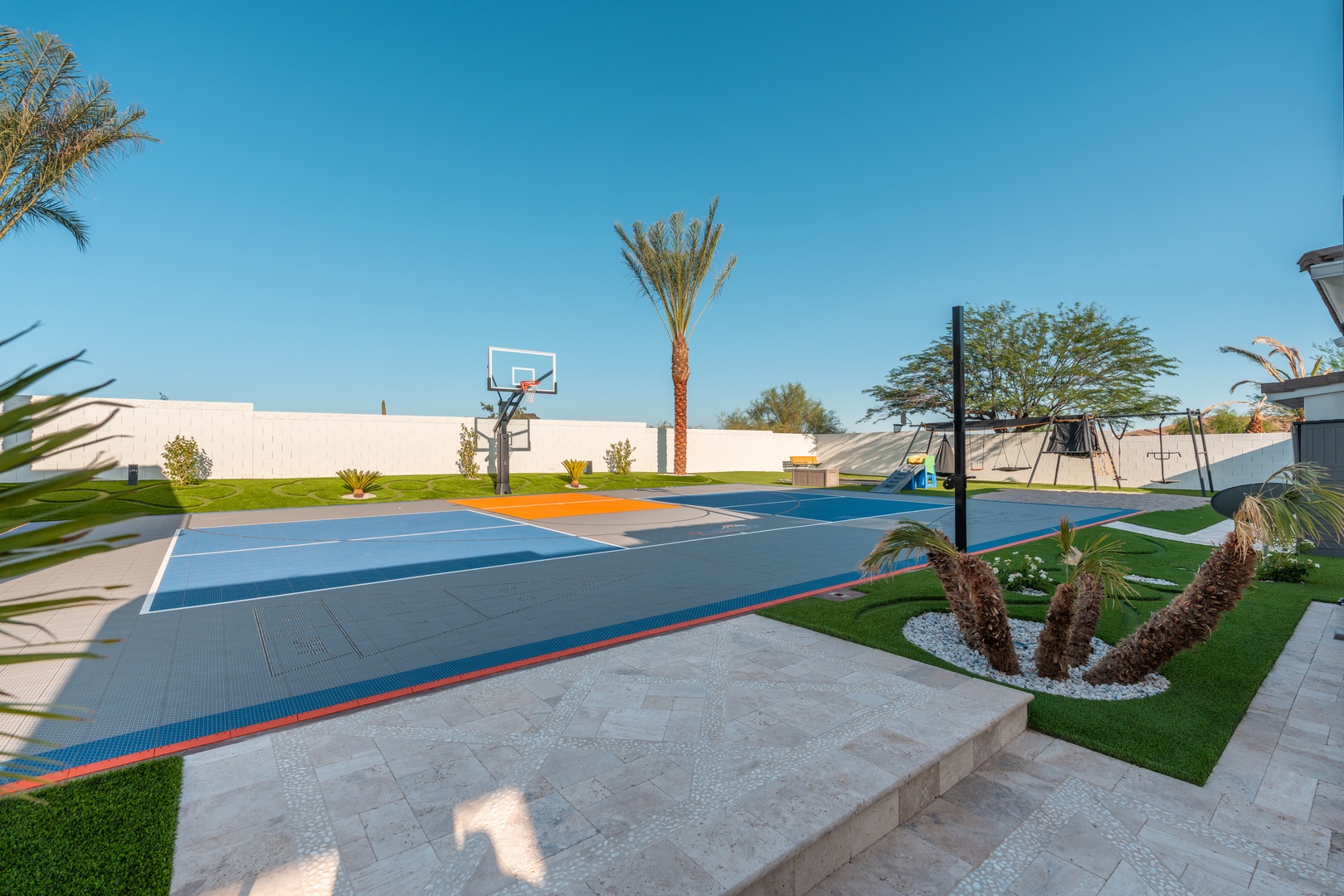 Private outdoor recreation area featuring a full-size basketball court, landscaped gardens with palm trees, and children's playground—perfect for active family fun under clear desert skies.