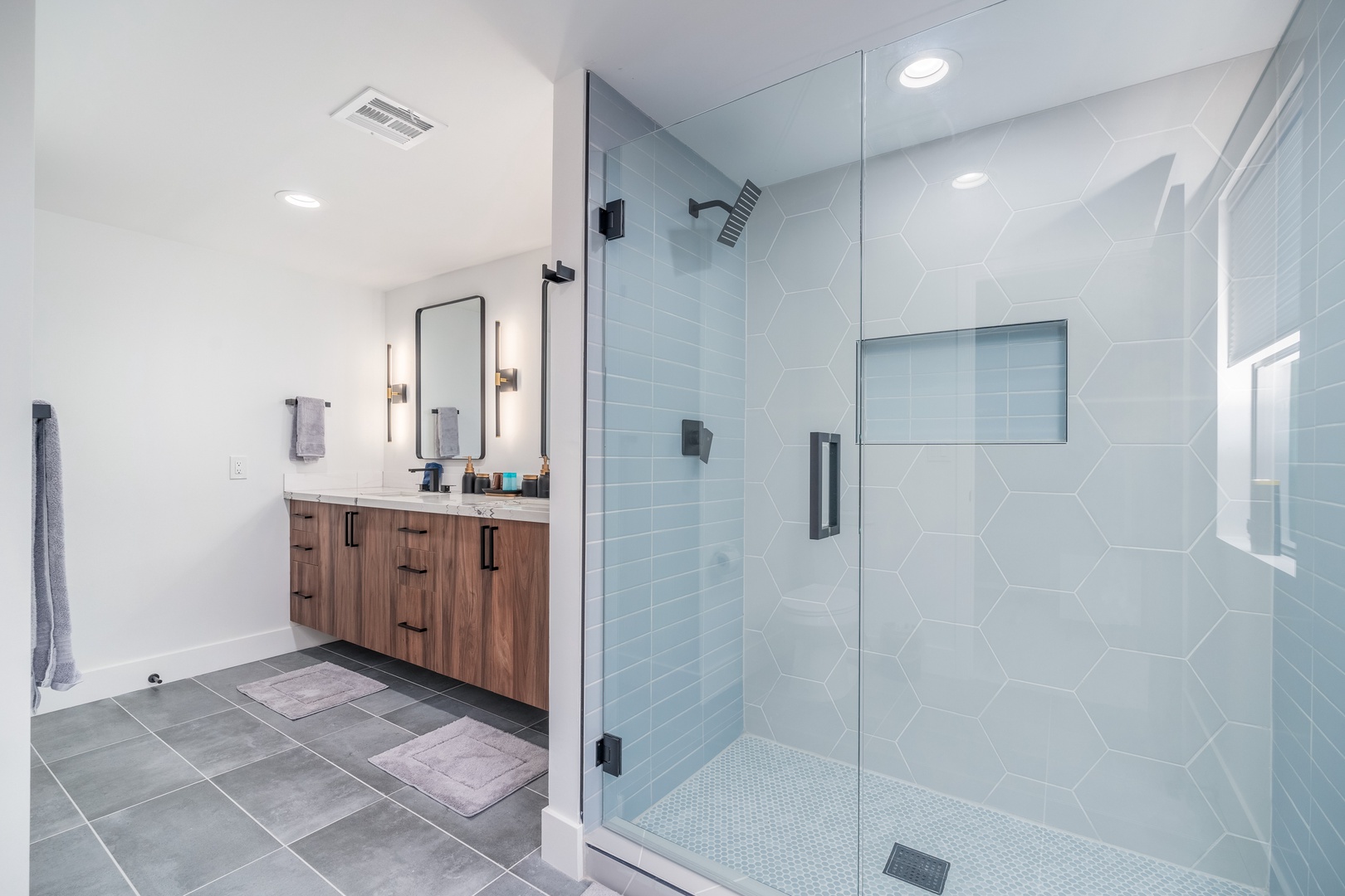 Unwind in your spa-inspired bathroom with a stunning walk-in shower featuring modern geometric tilework, dual vanities, and thoughtful lighting—a serene retreat designed for your comfort and relaxation.