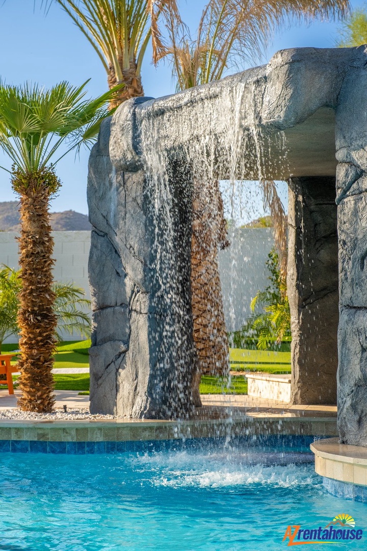 Dive into luxury with this stunning pool featuring a dramatic stone waterfall, surrounded by swaying palms under endless blue skies.