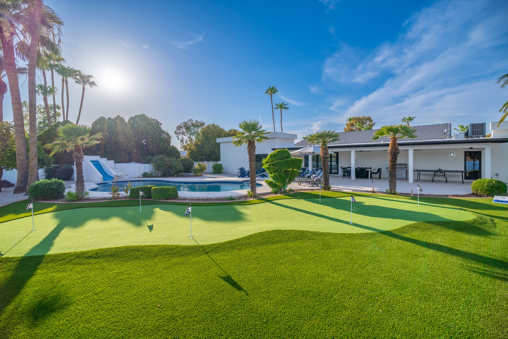 A modern desert escape features a private putting green, sparkling pool, and manicured grounds framed by towering palms—your perfect backdrop for sunny days and outdoor leisure.