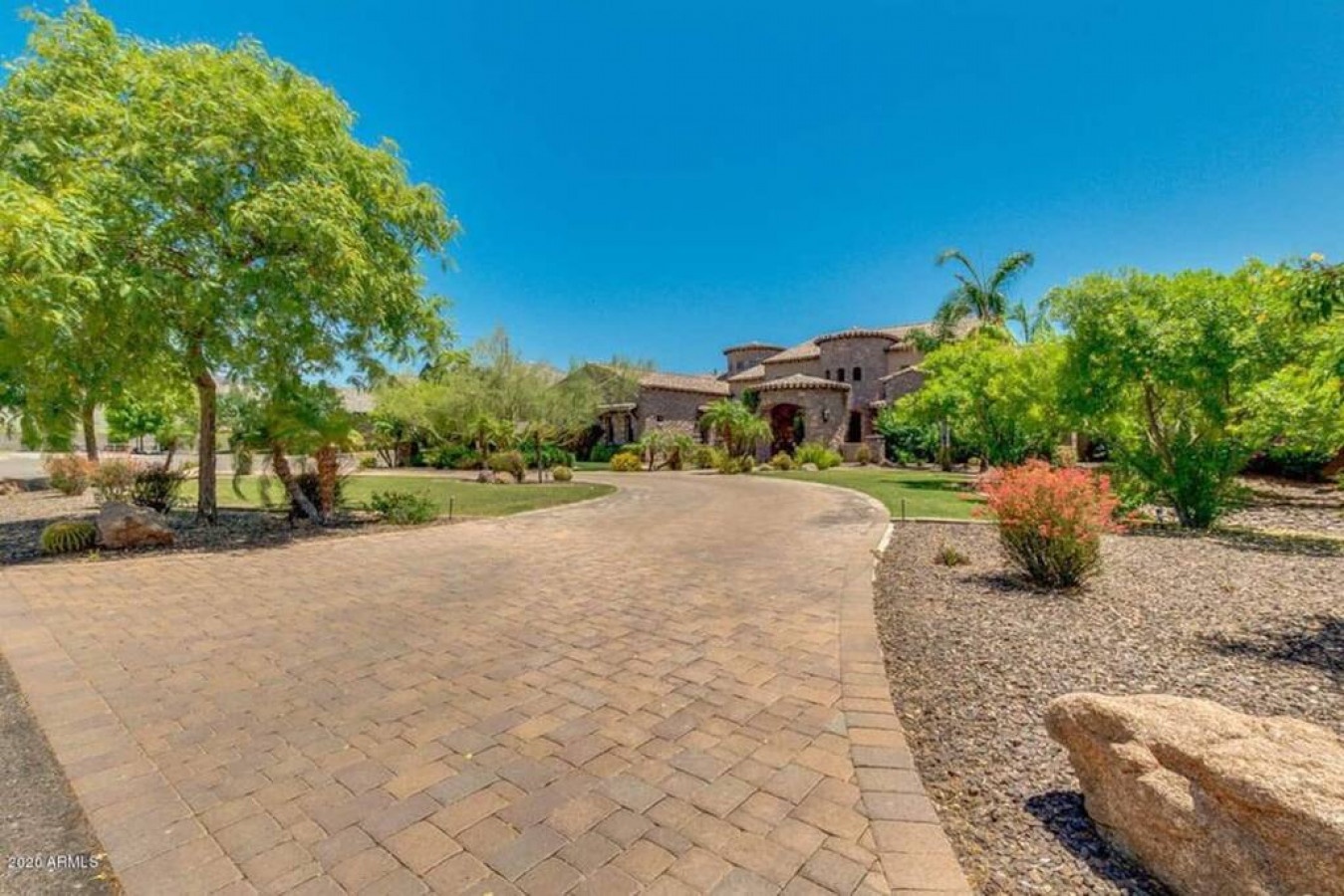 A stunning desert estate featuring Mediterranean architecture surrounded by mature desert landscaping and expansive outdoor spaces.