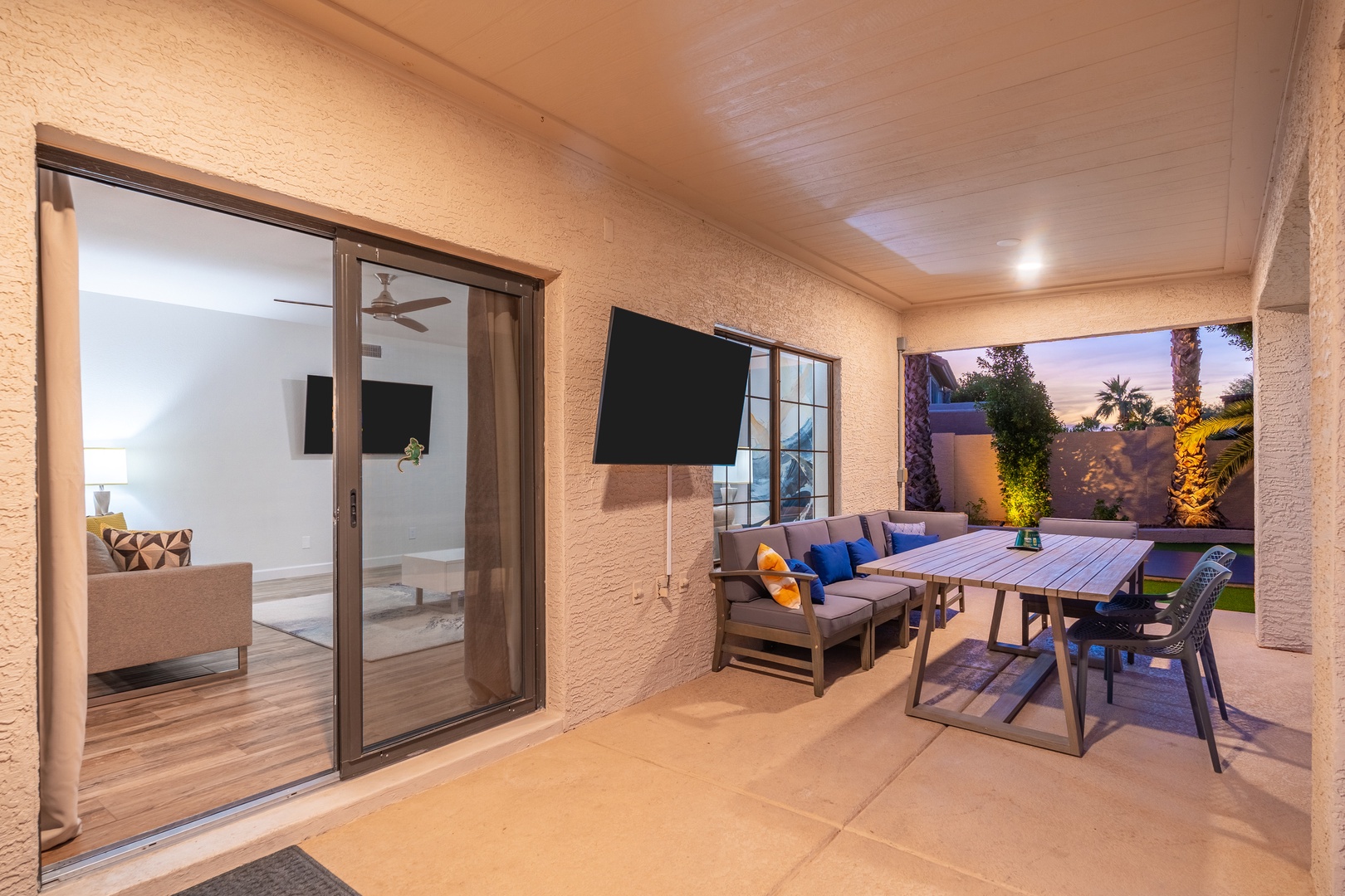 Your covered patio invites relaxation with cozy seating, a dining table for alfresco meals, and warm lighting, all opening to a beautifully lit backyard perfect for evening gatherings.