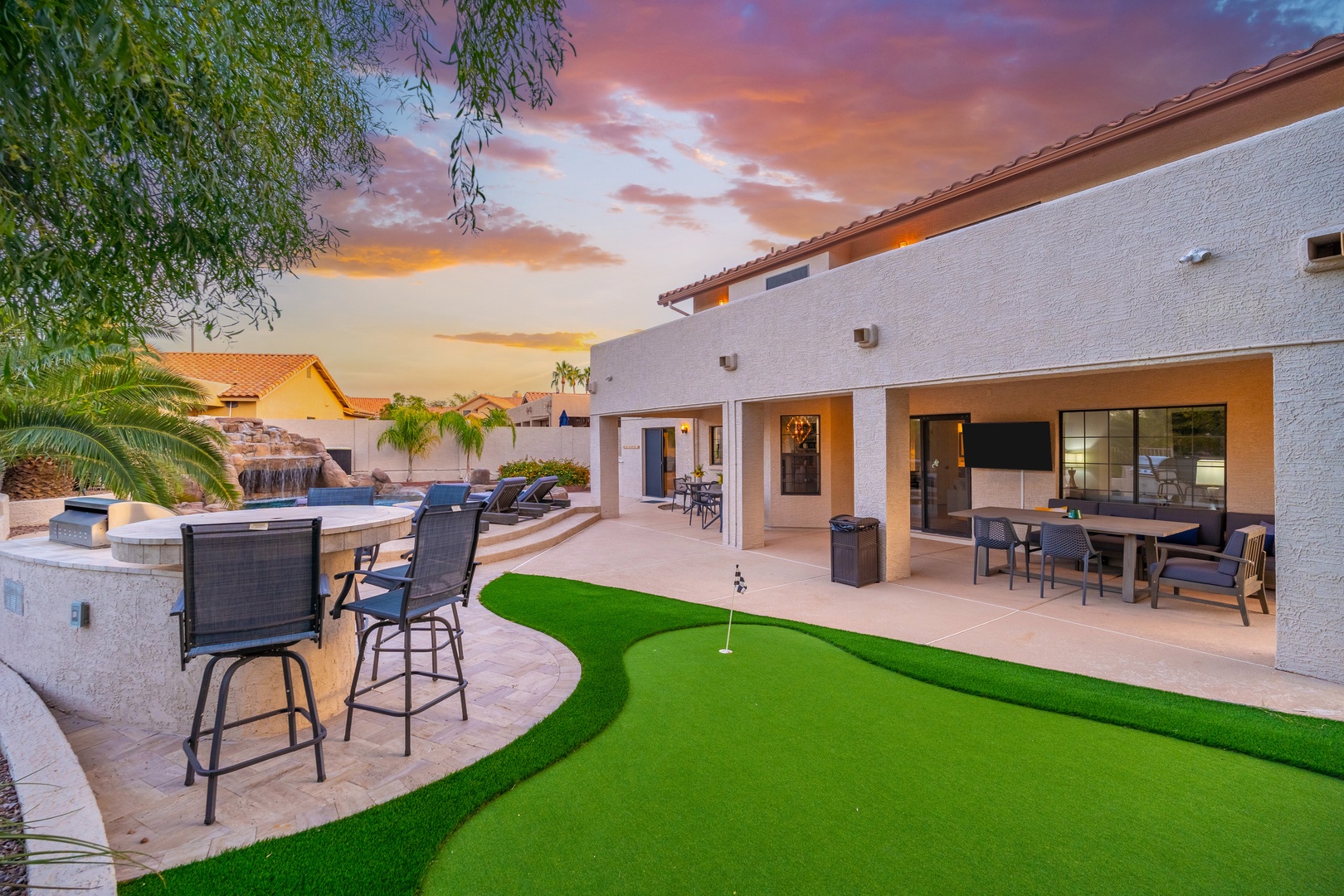 This backyard oasis offers everything for your perfect vacation. A stunning sunset paints the sky as you enjoy the putting green, outdoor seating, and pool access steps away.