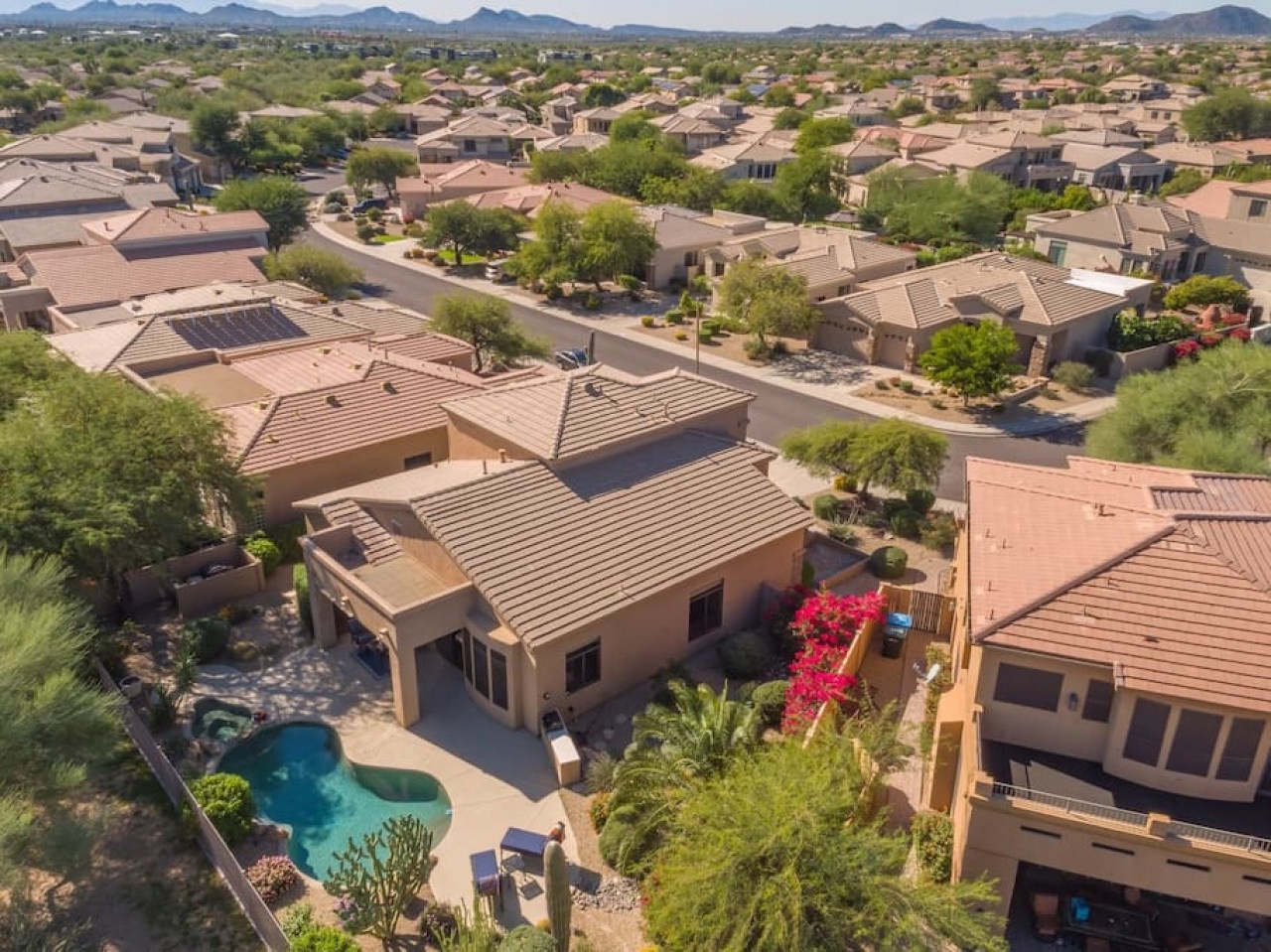Aerial view of desert home community with mountain backdrop and residential swimming pools throughout the neighborhood.