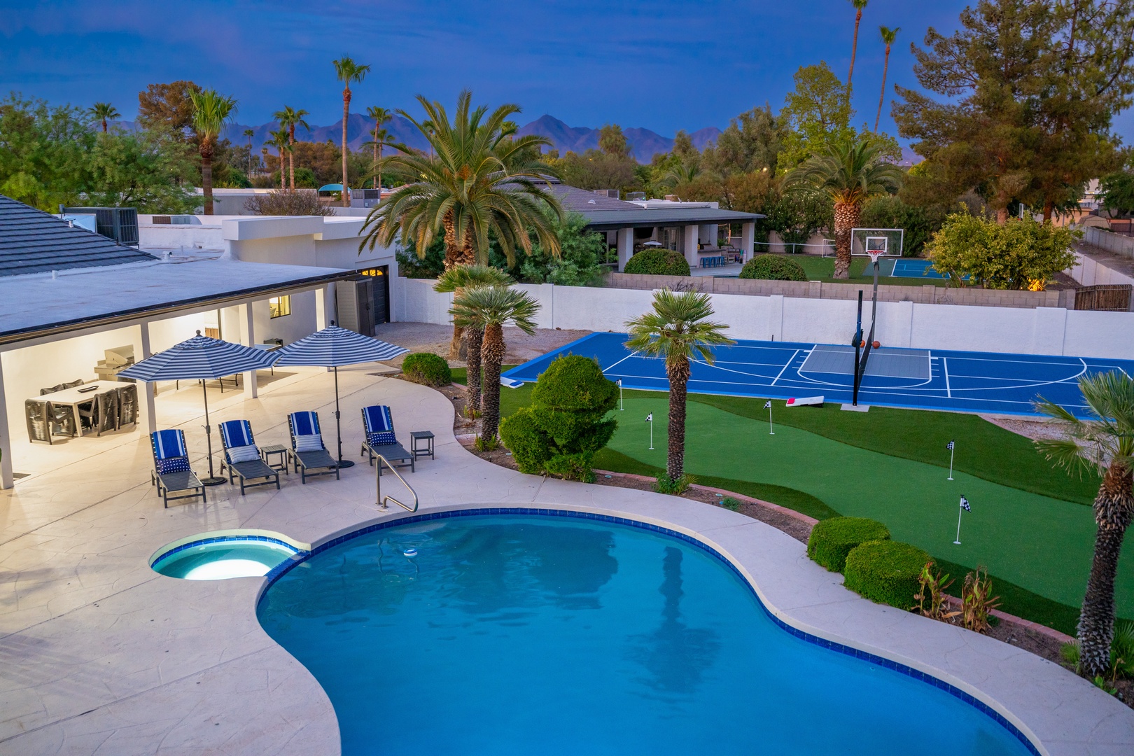 The property features a resort-style outdoor recreation area surrounded by mature palm trees and mountain views, complete with a basketball court, putting green, and pool with integrated spa.
