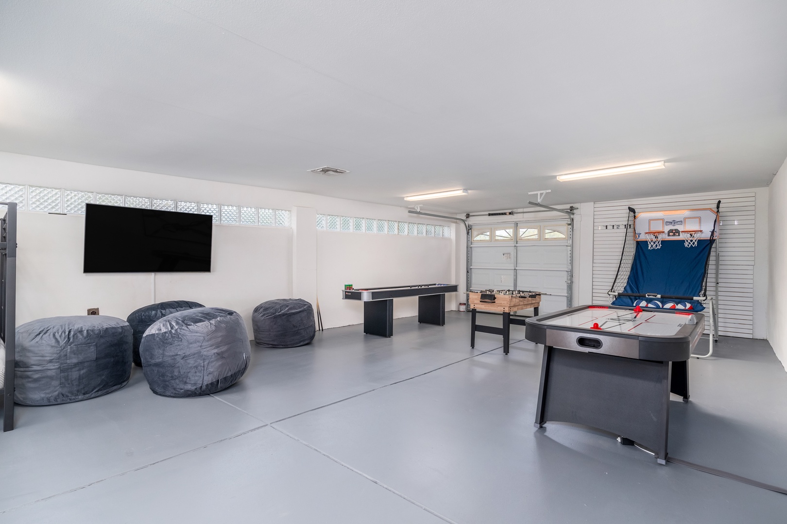 Your game on with friends or family in this spacious entertainment room featuring cozy bean bag seating, a large screen TV, air hockey, foosball, and a basketball shootout game for endless fun.