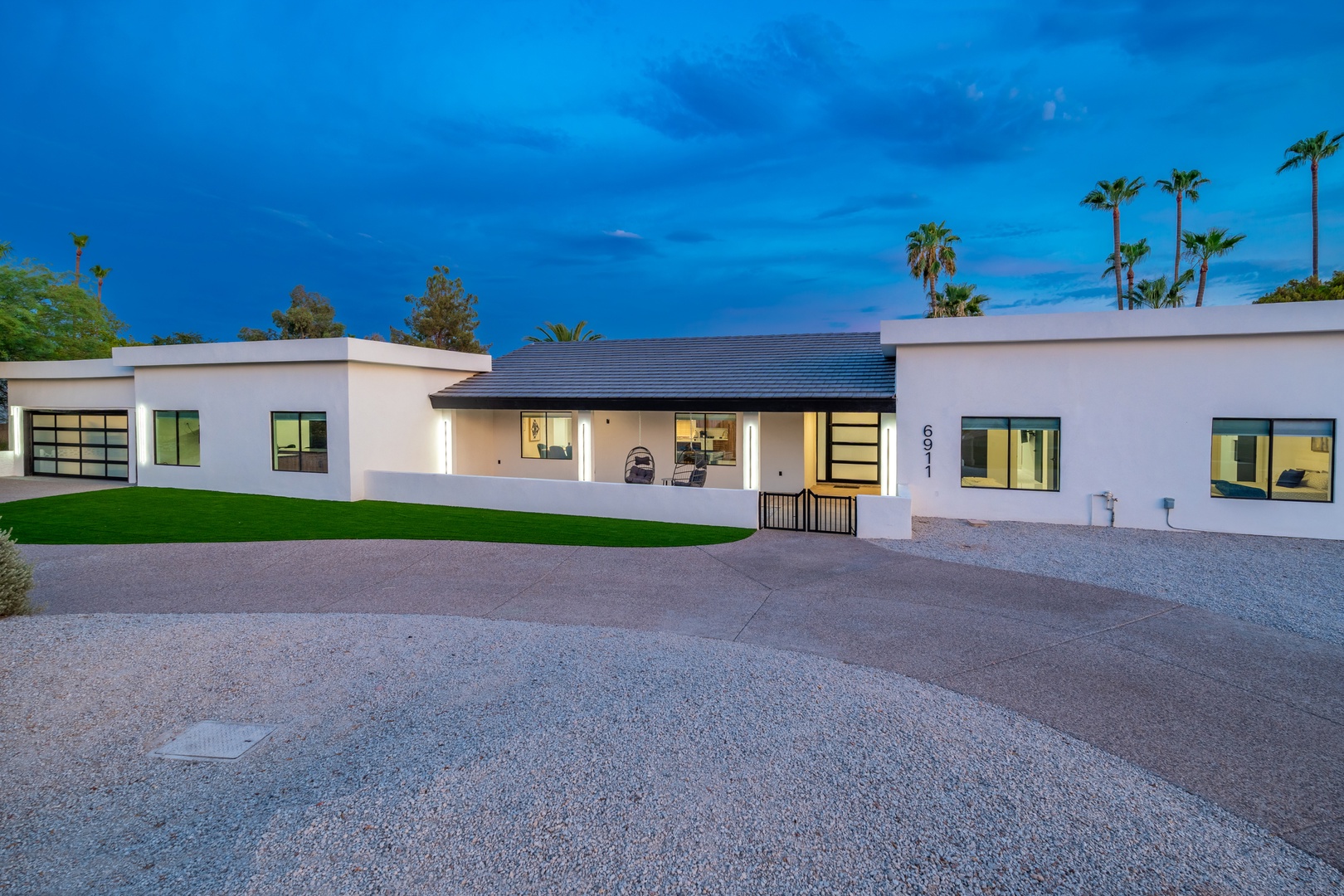 Contemporary desert retreat at twilight, featuring modern architecture, manicured lawn, and swaying palms against a dramatic evening sky—a serene desert oasis awaits.
