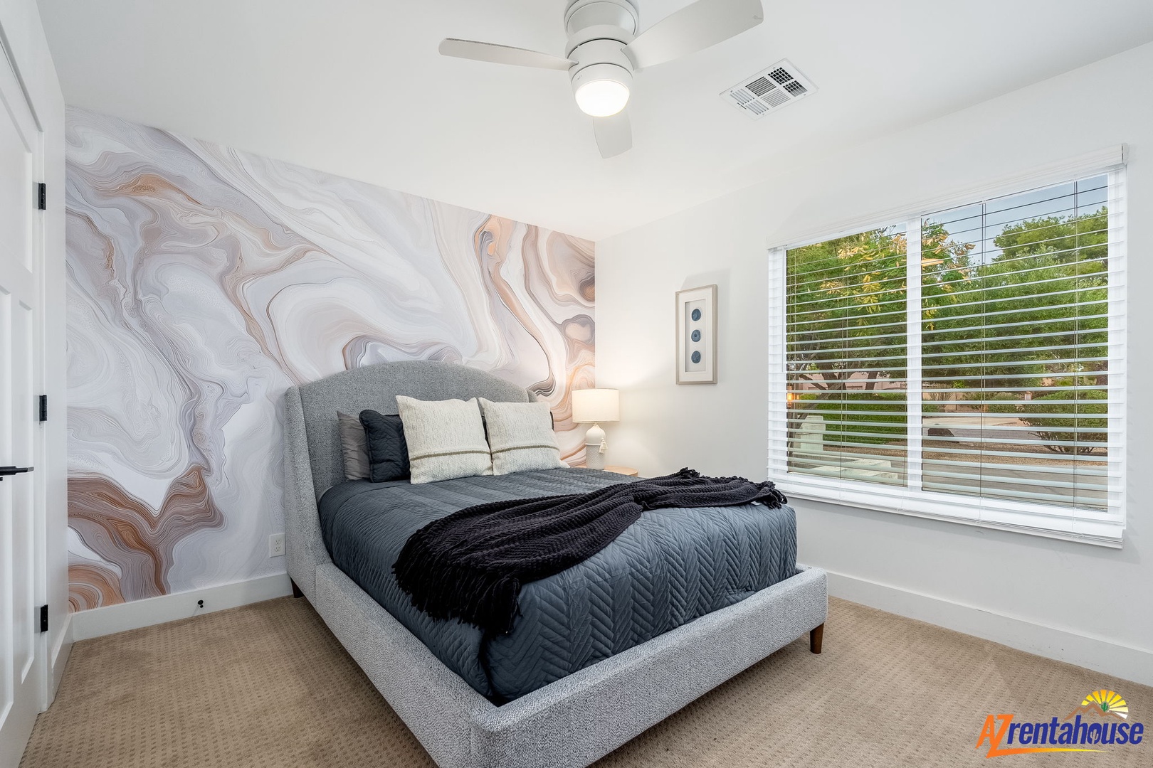 Drift off to sleep in your stylish bedroom featuring a stunning marble accent wall and peaceful garden views.