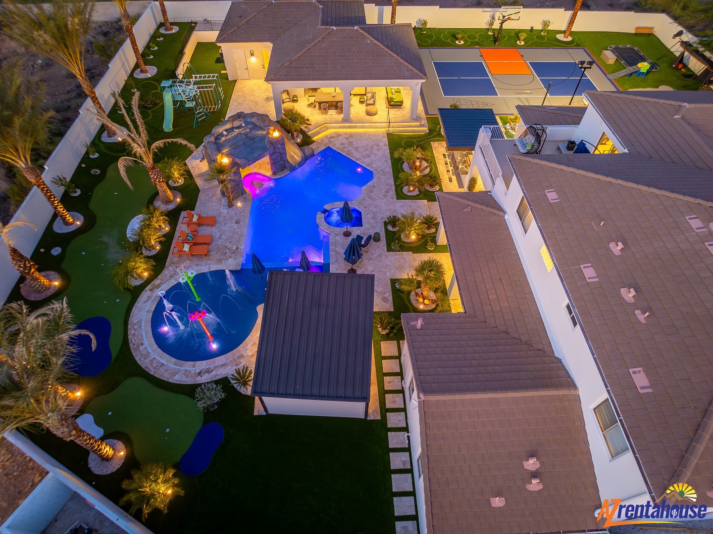 Aerial view of an impressive resort-style property featuring multiple pools, outdoor entertainment areas, and landscaped grounds illuminated for evening enjoyment.