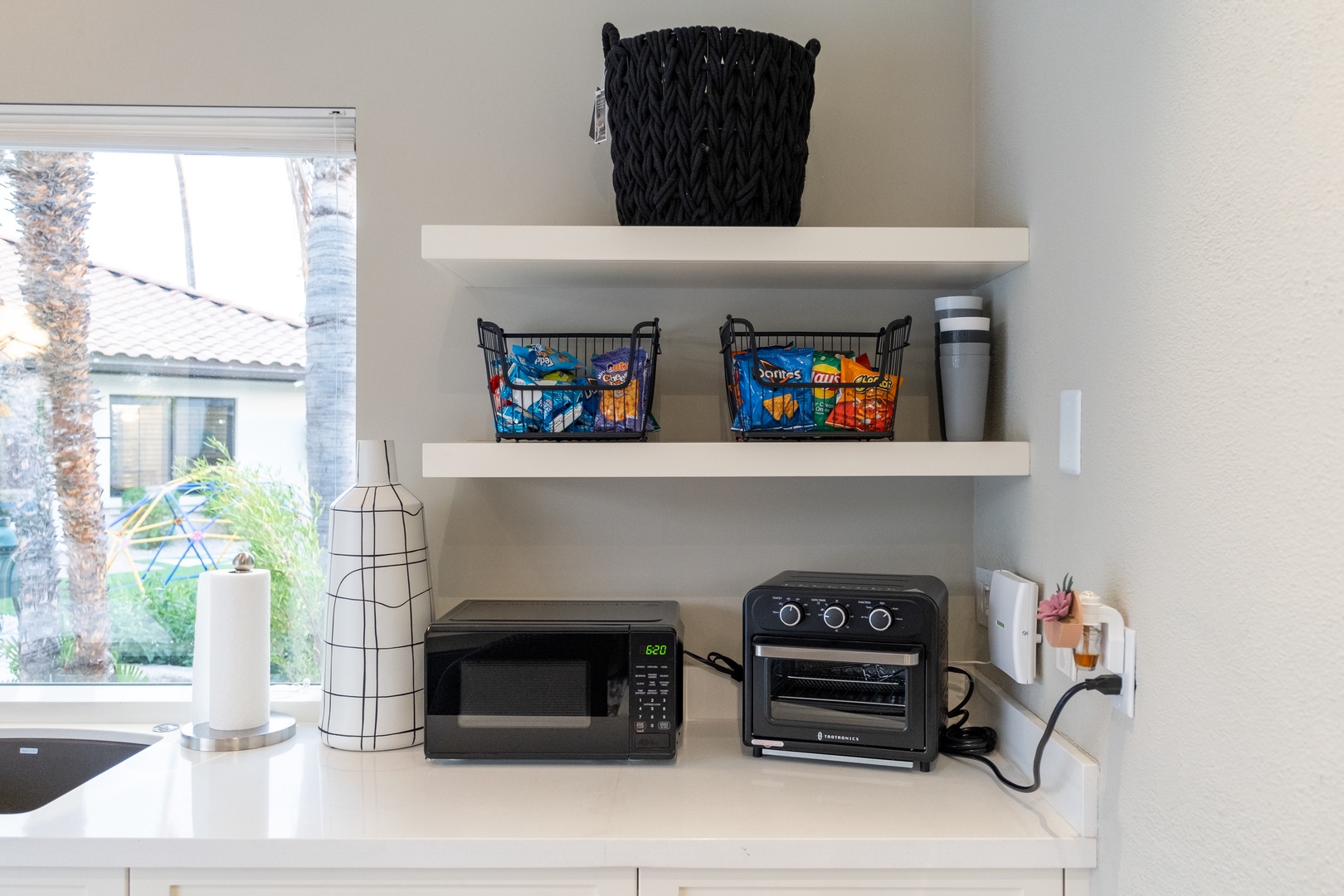 Your kitchenette comes fully equipped with a microwave and countertop oven, plus snacks and essentials neatly organized on floating shelves for your convenience.