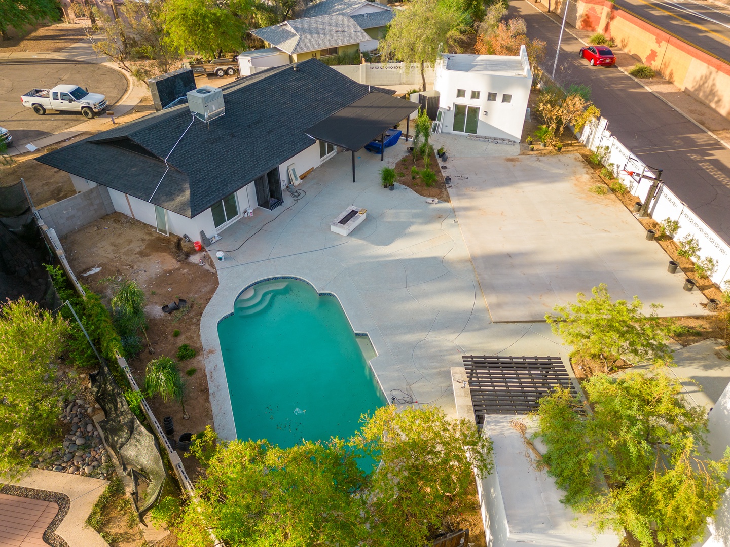 Aerial view of a modern vacation rental featuring a sparkling swimming pool, spacious patio, and lush greenery in a quiet residential neighborhood.