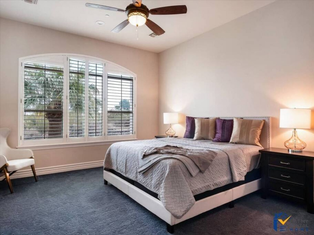 Sink into your plush bed with crisp linens and soft accent pillows. Natural light filters through elegant shutters, while bedside lamps offer a warm glow for evening relaxation in your serene retreat.