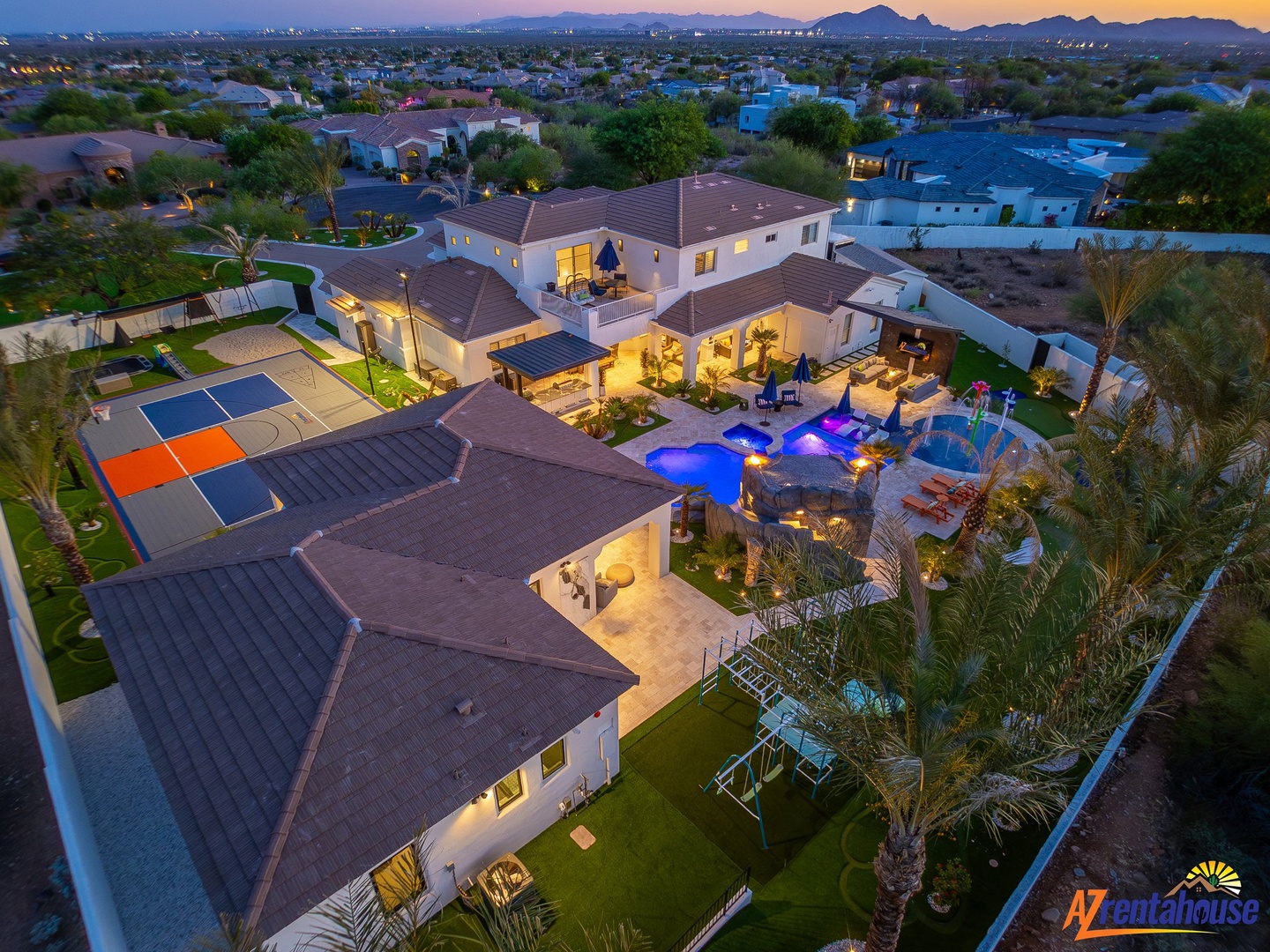 Stunning estate showcasing a luxury home with expansive outdoor amenities set against desert mountains at twilight.