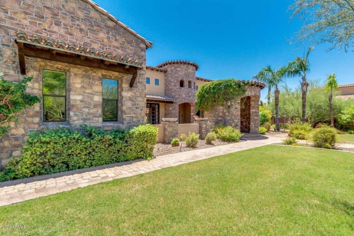 Stunning stone-clad Mediterranean villa with manicured lawns and desert landscaping creates an elegant arrival experience.