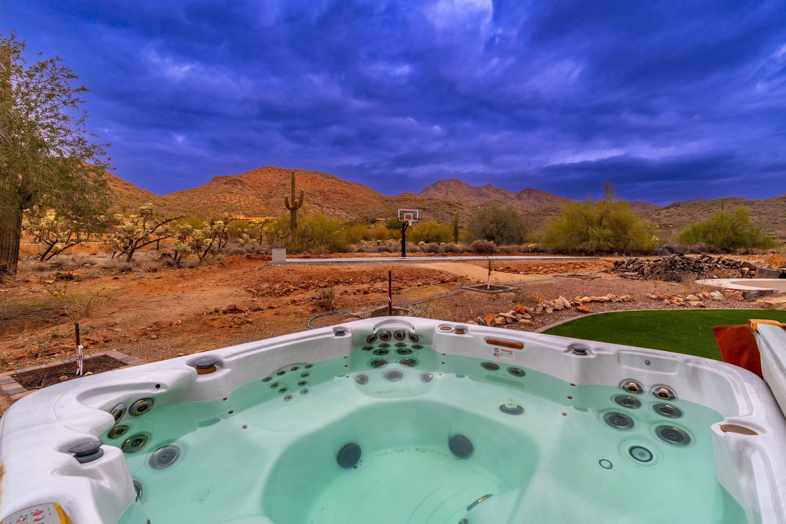 Soak in the hot tub as dramatic desert mountains and saguaro cacti frame the horizon—a stunning backdrop at twilight for complete outdoor relaxation.