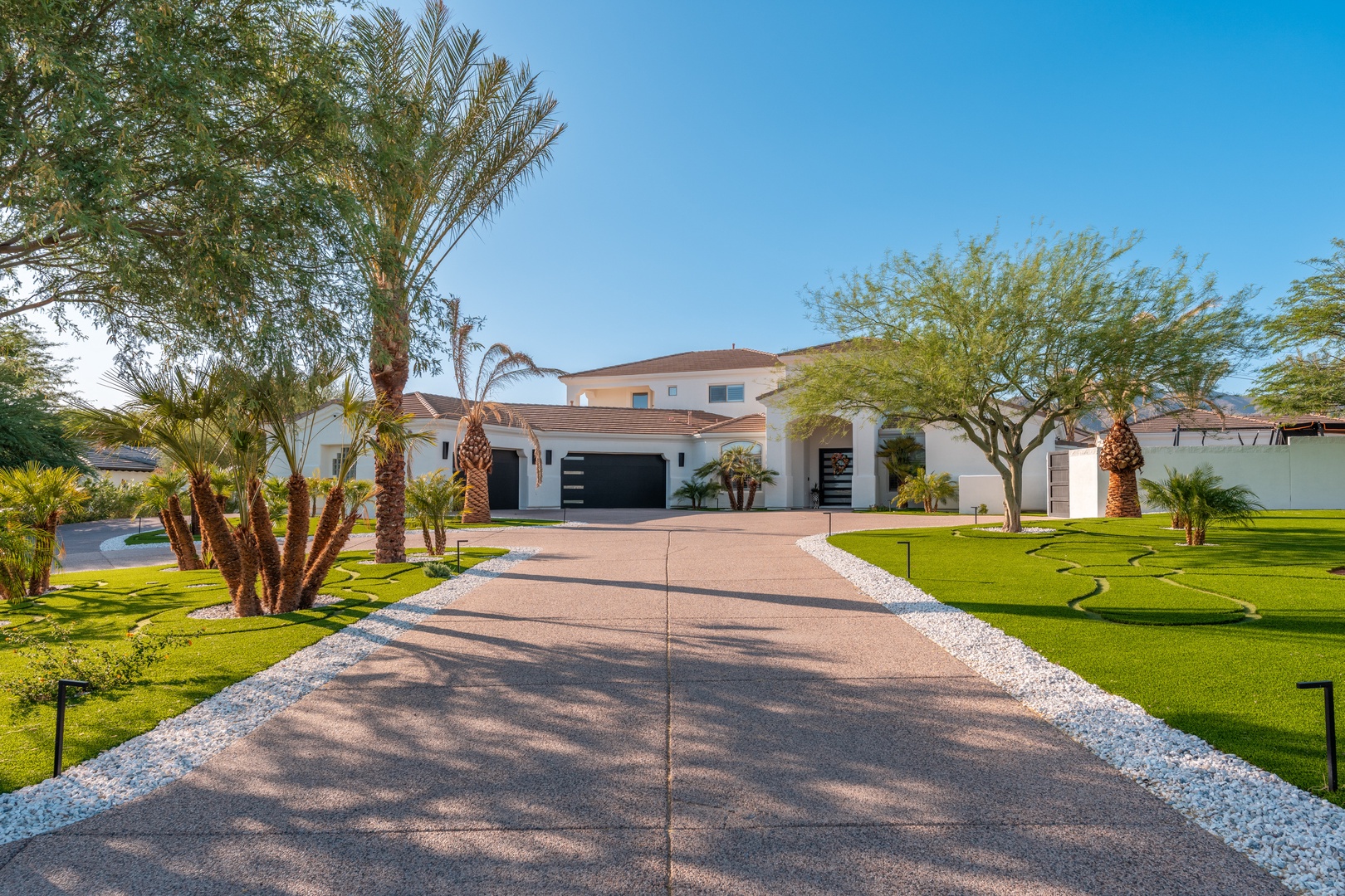 Modern desert retreat set amid lush landscaping with palm trees and manicured lawns, featuring a spacious driveway leading to the private entrance.