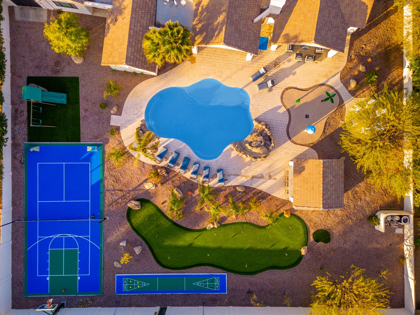 Aerial view of the property reveals an extensive recreation area with a freeform swimming pool, sports courts, mini-golf course, and sun-drenched lounging zones surrounded by tropical palms.