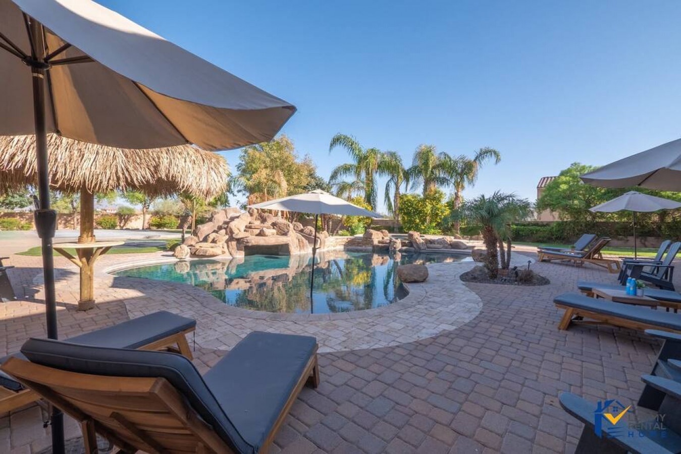 Unwind by your private lagoon-style pool with rock waterfall, tropical palms, and cushioned loungers under desert sunshine.