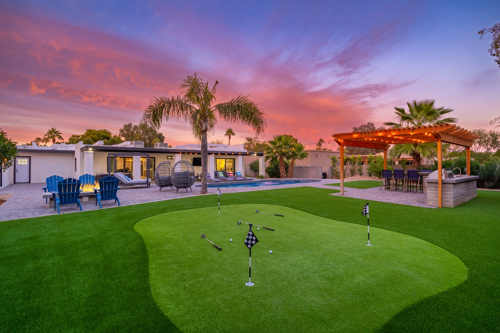 Stunning resort-style backyard featuring private putting green, sparkling pool, covered patio with dining, lounging areas, and vibrant sunset skies—perfect for relaxation and entertainment.