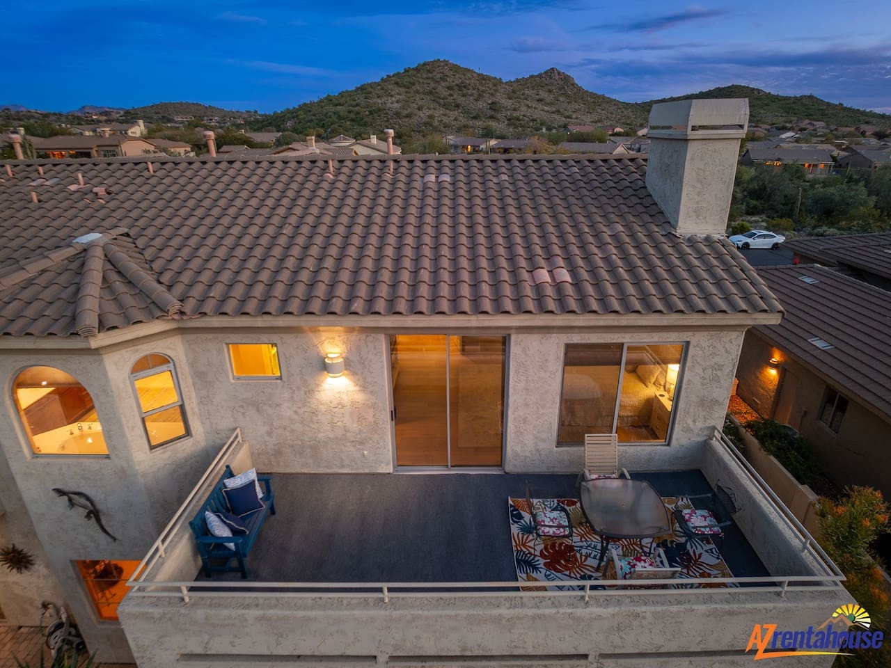 Stunning desert mountain property featuring a private rooftop terrace with comfortable outdoor seating, surrounded by scenic desert hills and twinkling neighborhood lights at dusk.