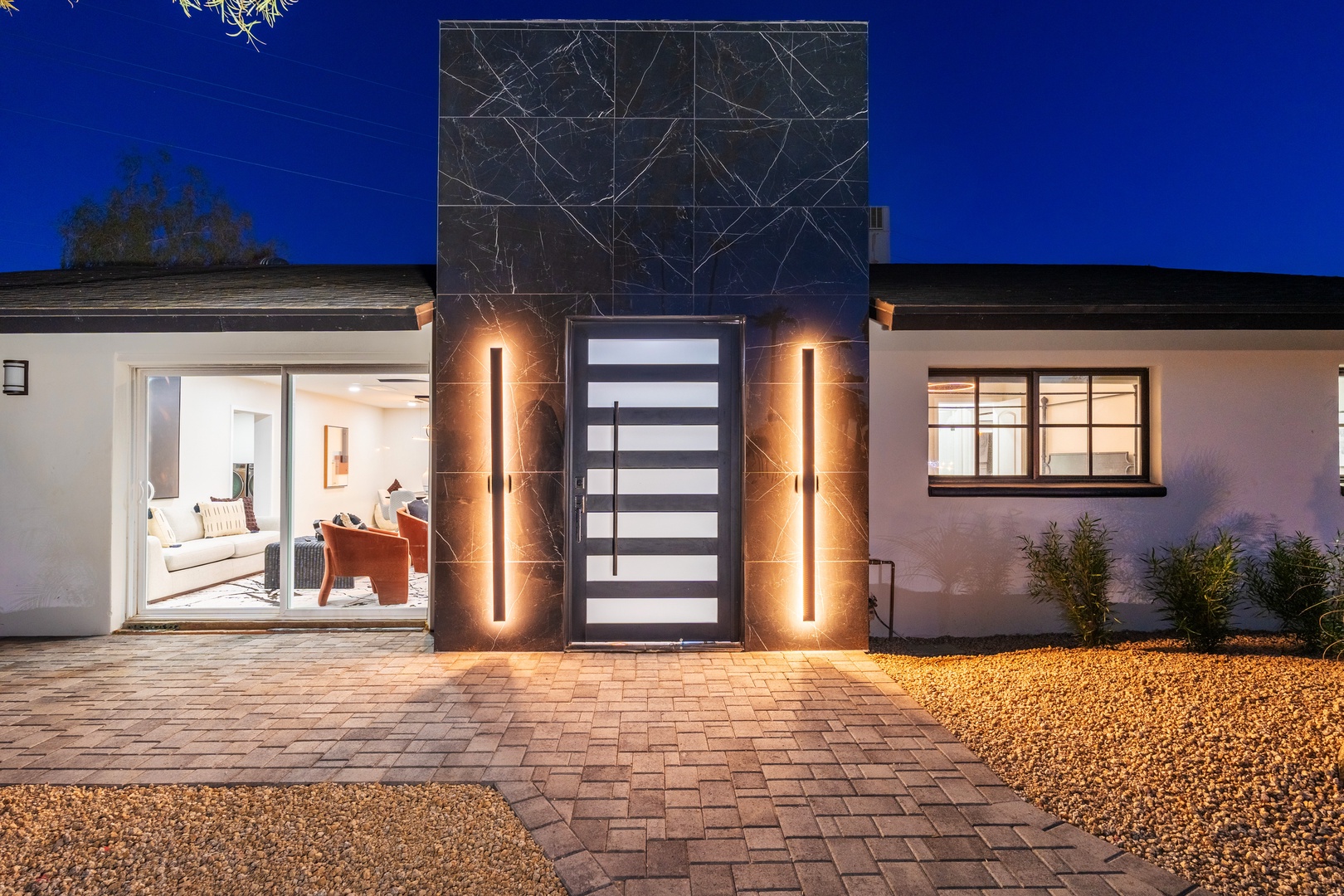 Modern elegance greets visitors at this contemporary home featuring sleek architectural design, illuminated vertical light fixtures, and carefully curated landscaping under a vivid evening sky.