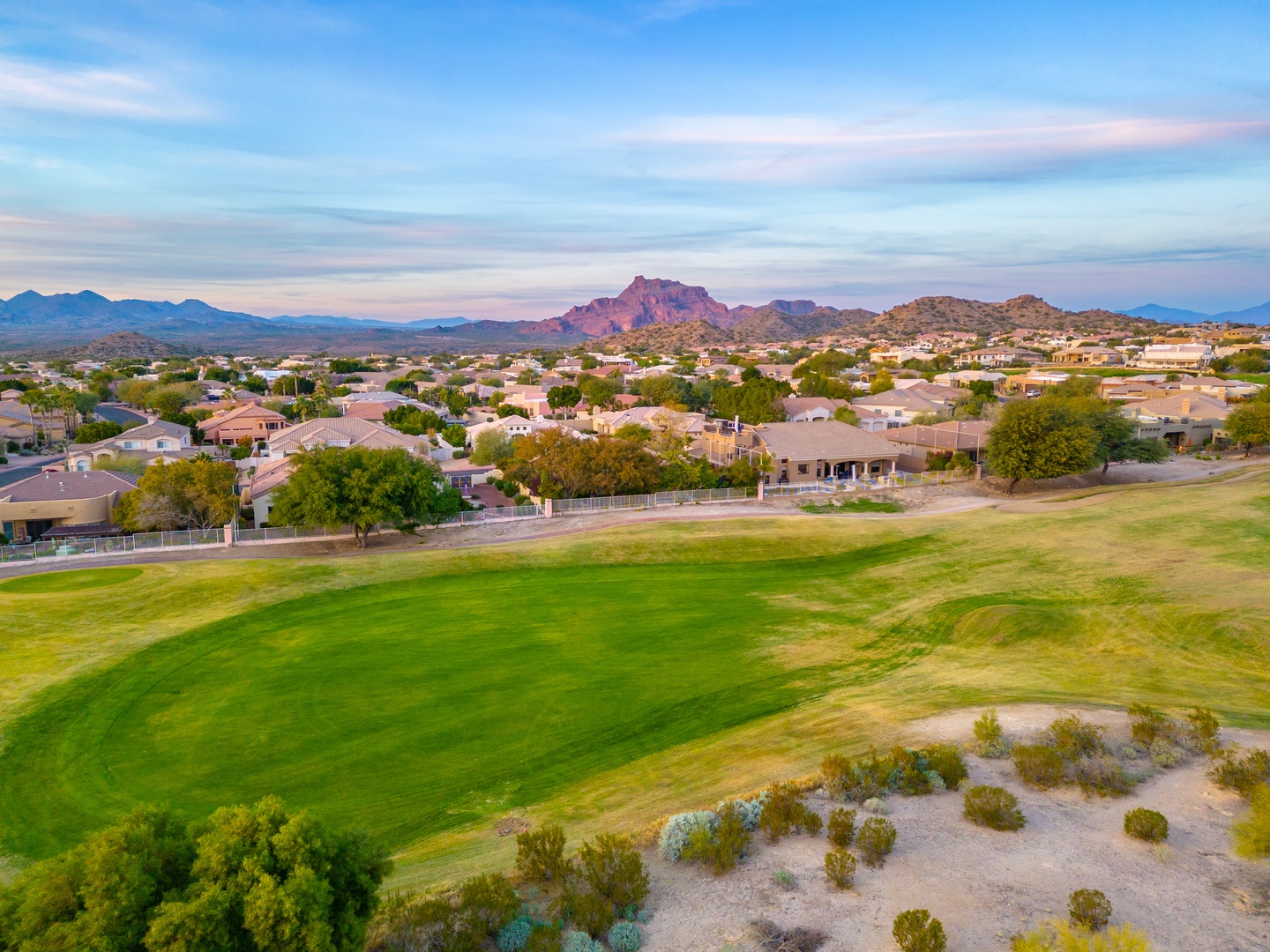 Aerial view of the property's scenic desert community with manicured golf course fairways and dramatic mountain backdrop at sunset.