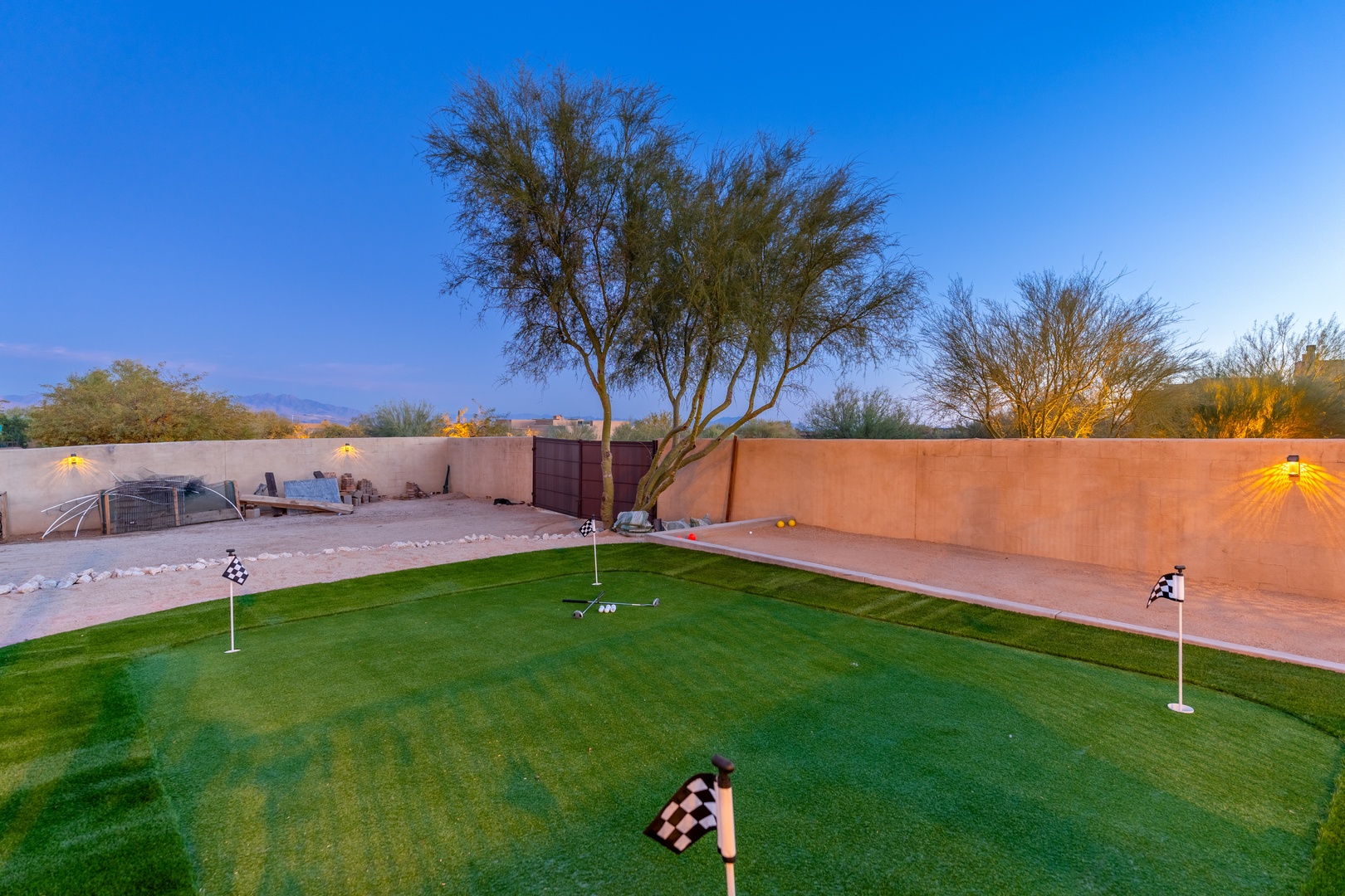 A private putting green set beneath desert skies and mature trees, part of the property's outdoor amenities in a walled backyard setting.